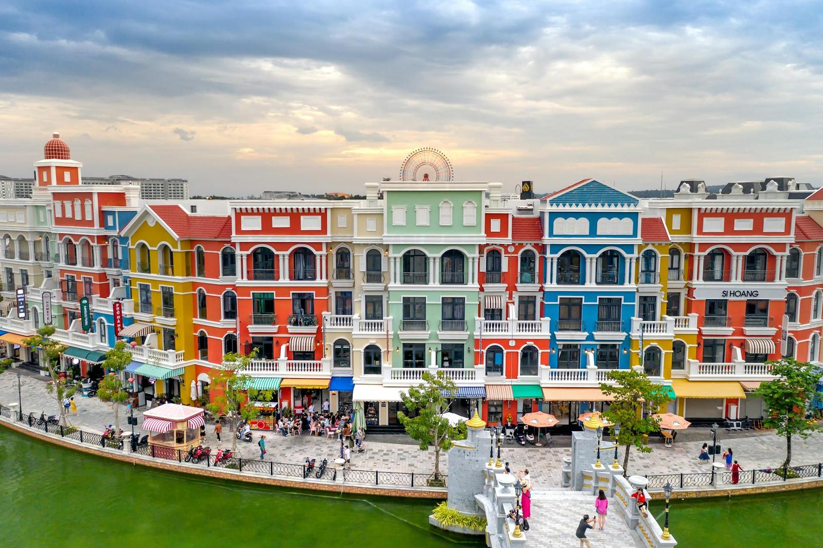 A row of colorful colonial-style waterfront buildings with people strolling below