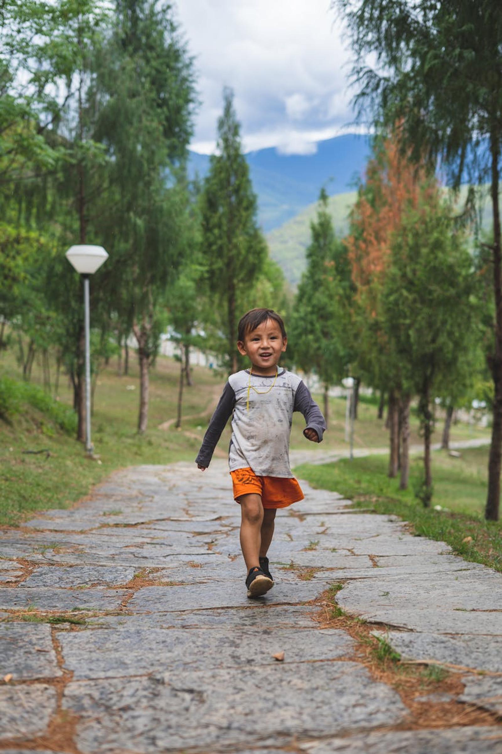 A happy child walking on a stone path surrounded by lush greenery in the mountains of Paro, Bhutan
