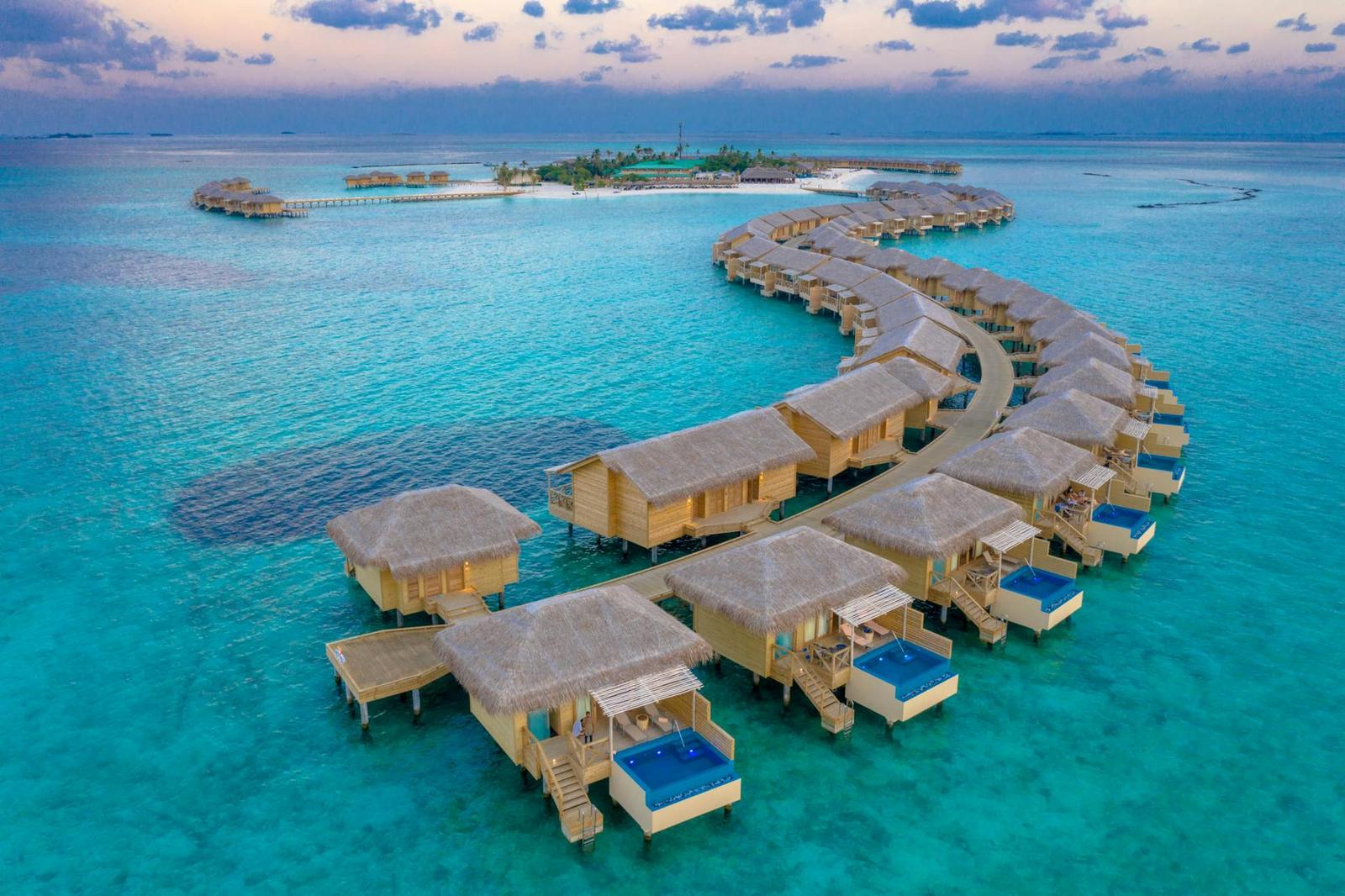 A curved chain of overwater villas seen from above at dusk