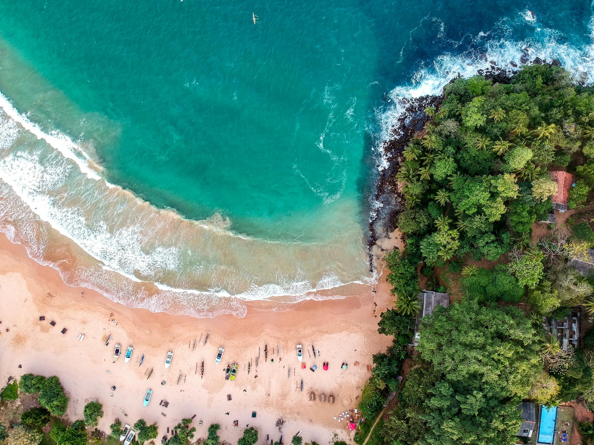 Aerial view of a crescent beach with boats and bathers beside a wooded point