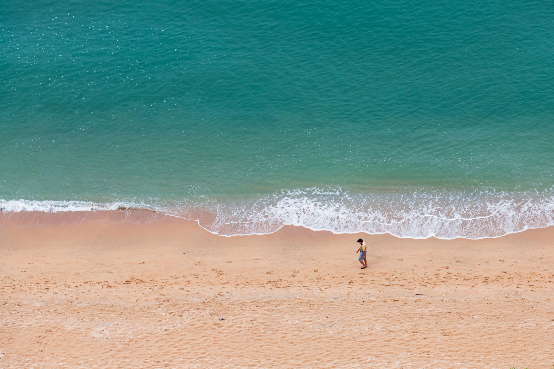 Aerial view of a serene beach in Pattaya City, Thailand, with a lone tourist walking