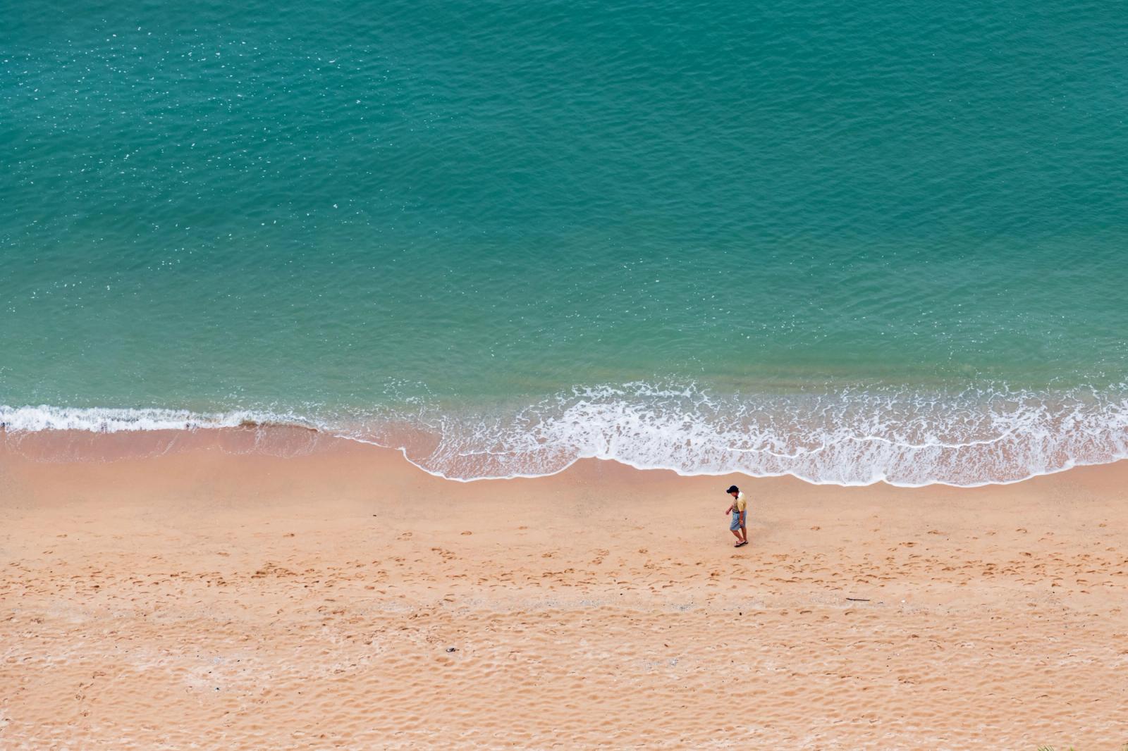 Aerial view of a serene beach in Pattaya City, Thailand, with a lone tourist walking
