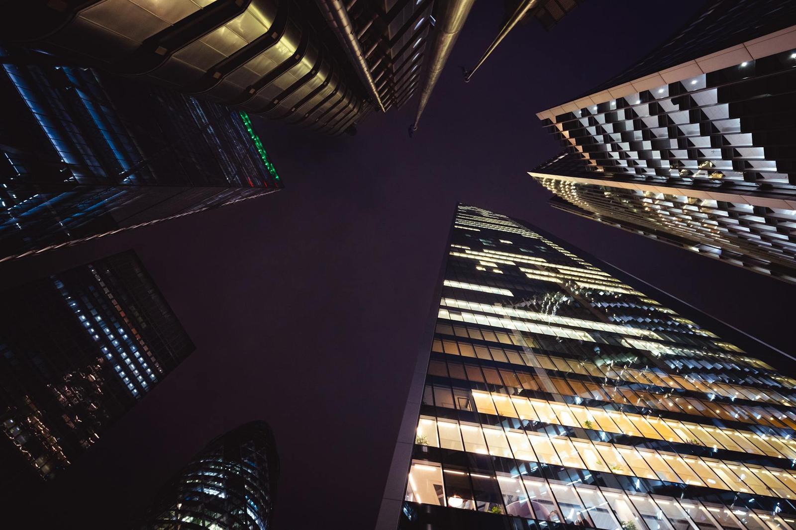 Looking up at illuminated glass skyscrapers converging against a night sky