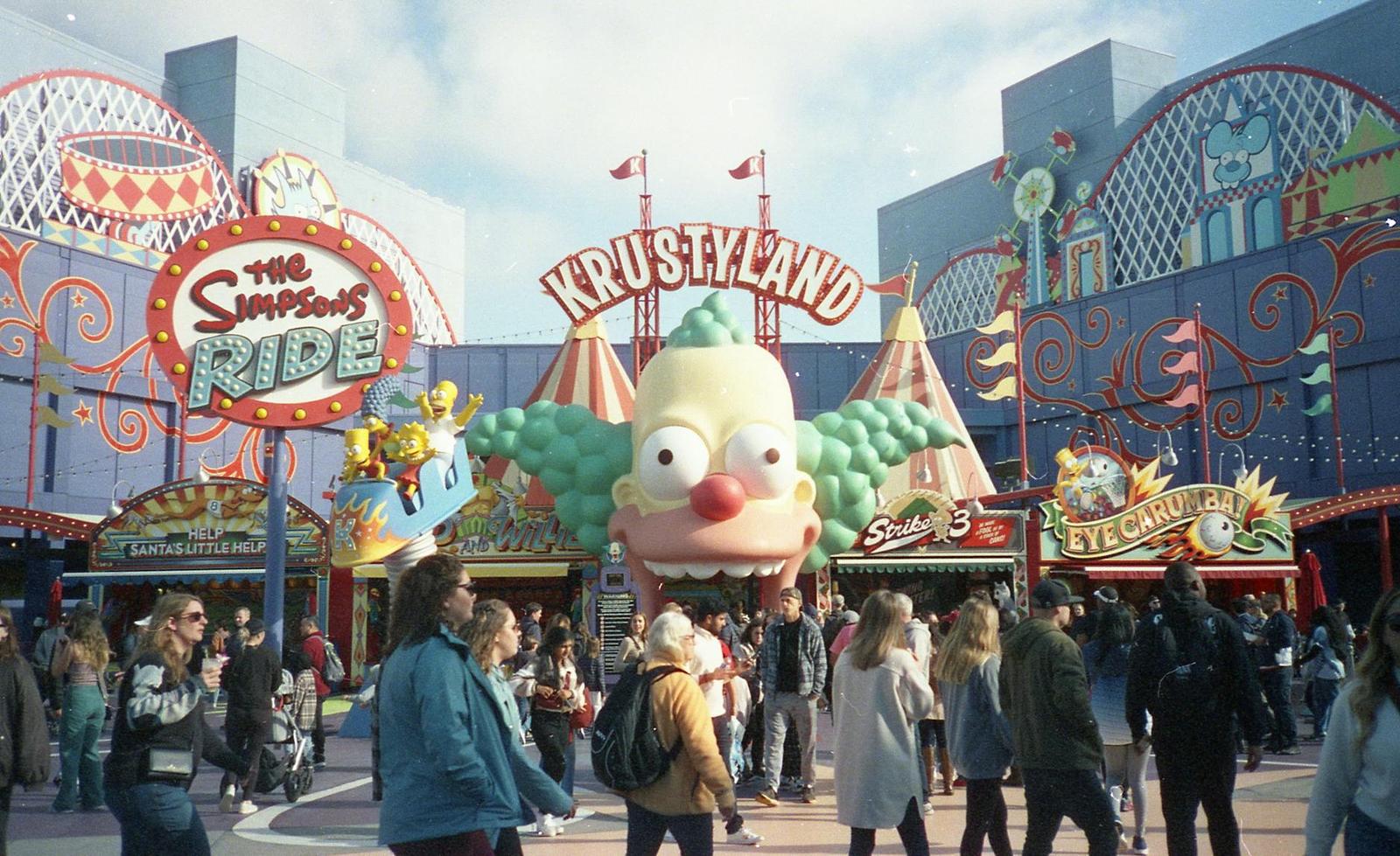 Crowds walking through a theme park entrance decorated with a giant cartoon clown face