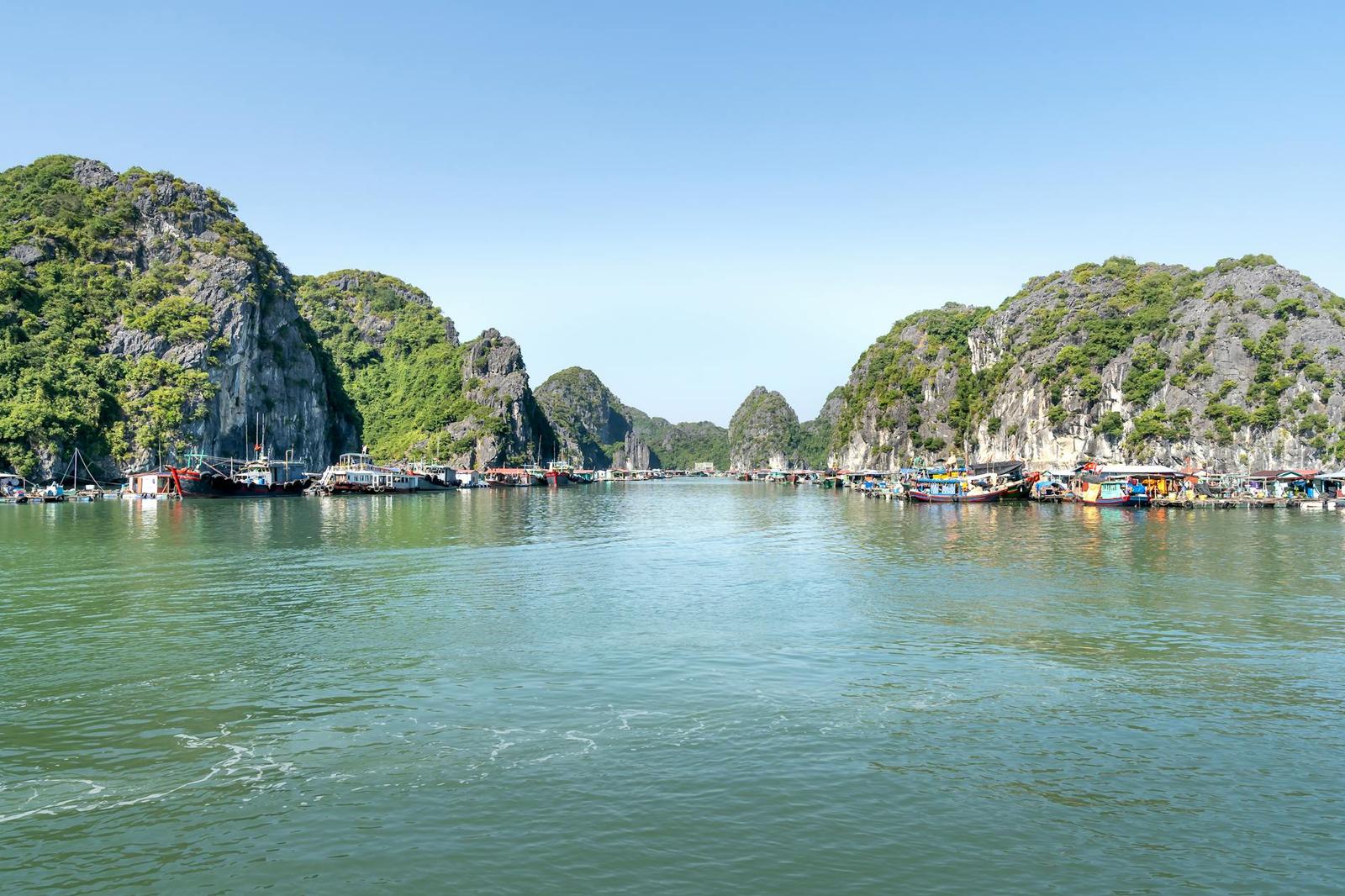 Limestone karst islands rising from calm green bay waters dotted with boats