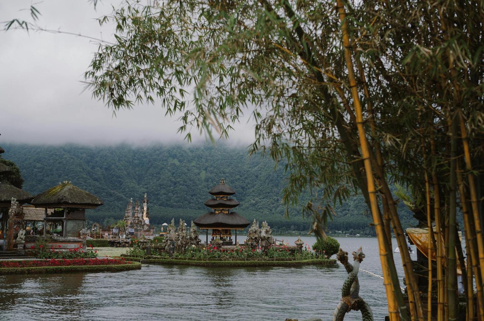 A tiered lakeside pagoda temple framed by bamboo with misty hills behind
