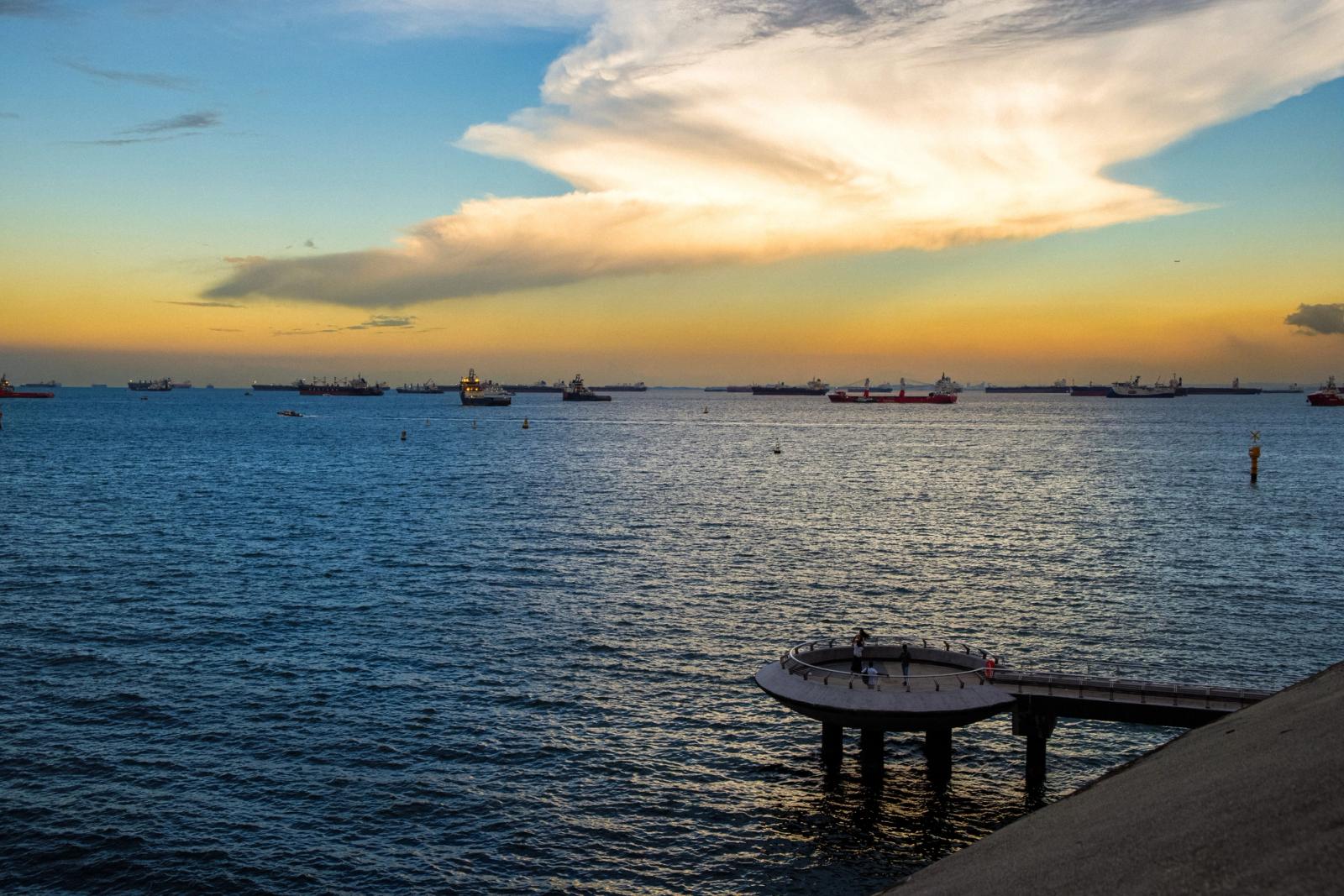 Serene sunset ocean view in Singapore with ships and wooden pier. Captures the beauty of evening tranquility