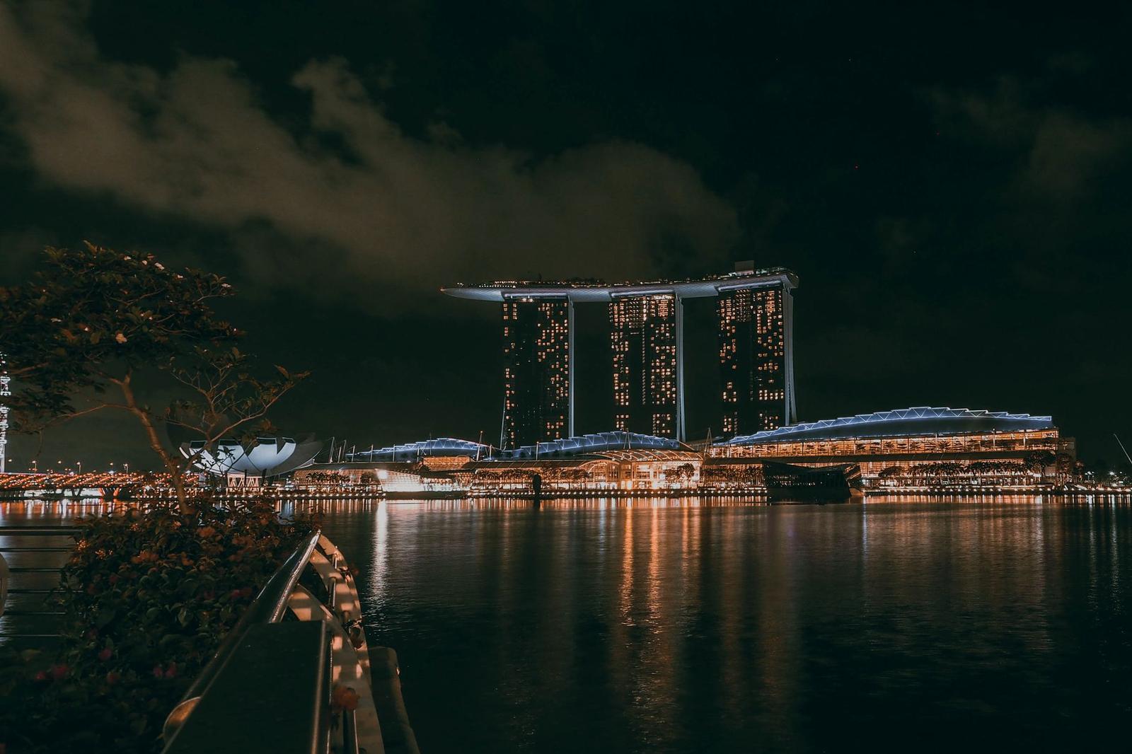 A lit hotel tower and waterfront reflected in dark water at night