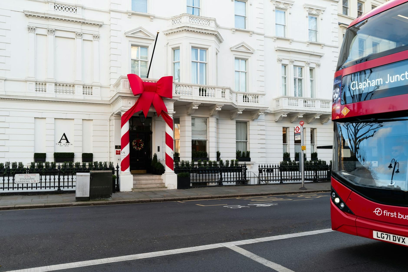 A white townhouse hotel entrance decorated with a giant red bow, a double-decker bus passing