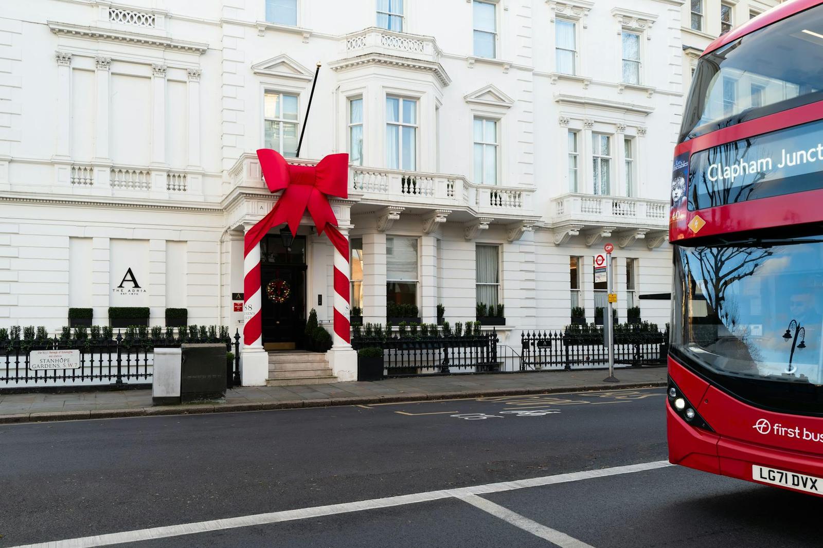 A white townhouse hotel entrance decorated with a giant red bow, a double-decker bus passing