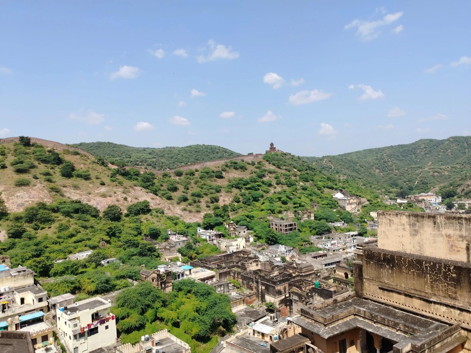 A panoramic view of lush green hills surrounding a rustic Indian village under a bright blue sky