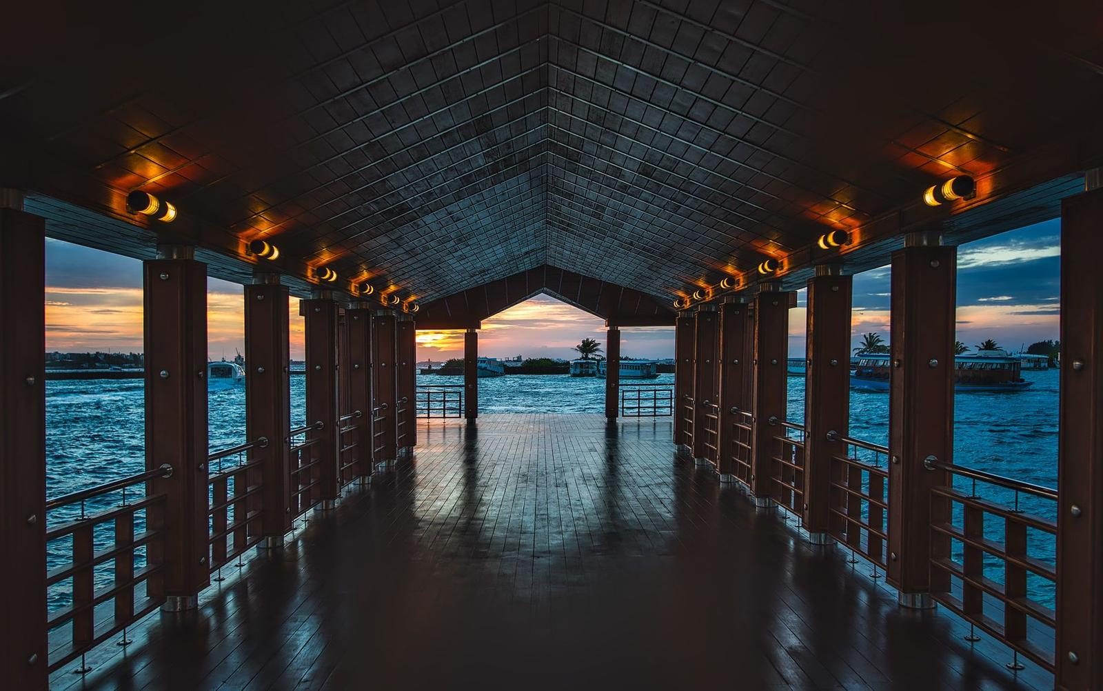 A covered wooden walkway framing an ocean sunset