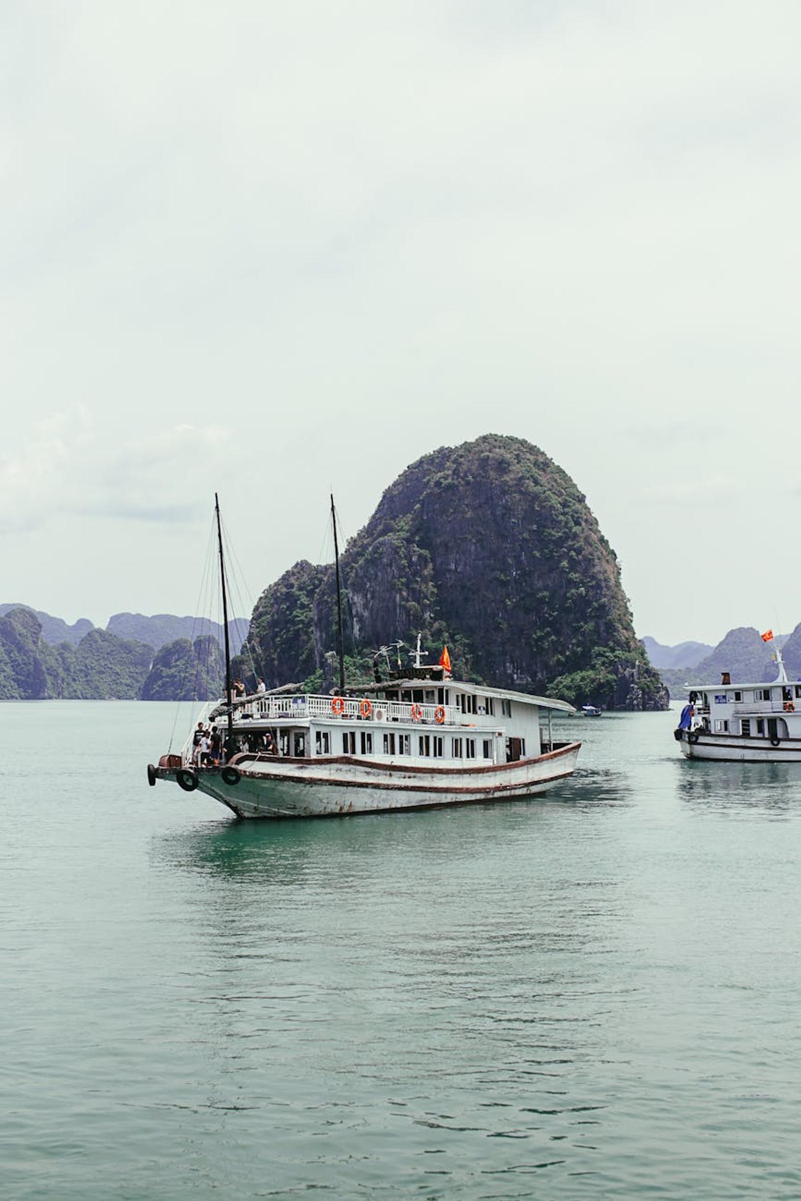 Two cruise boats passing a peaked limestone islet on calm water