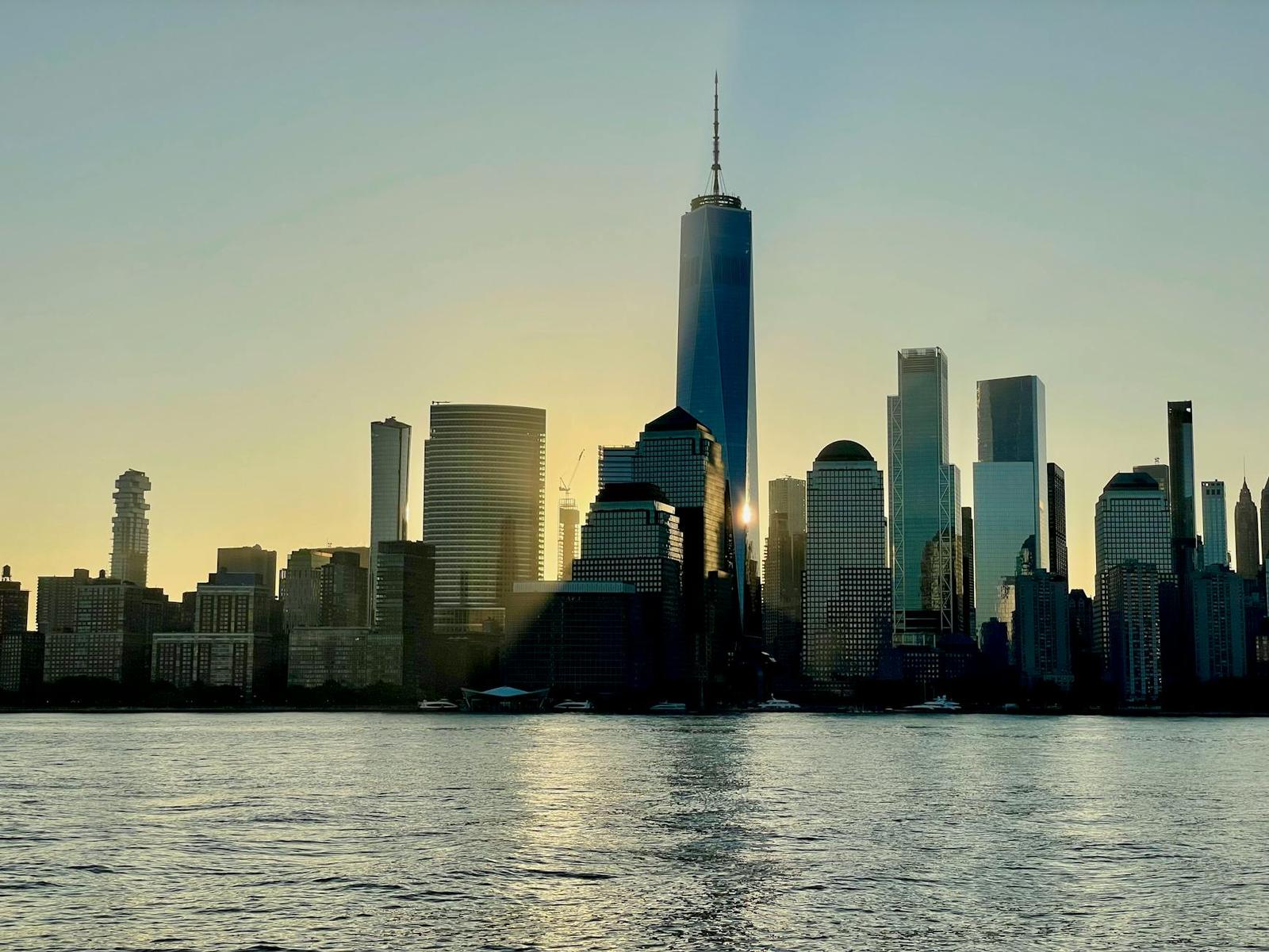 A waterfront skyline backlit by the sun with a tall central spire