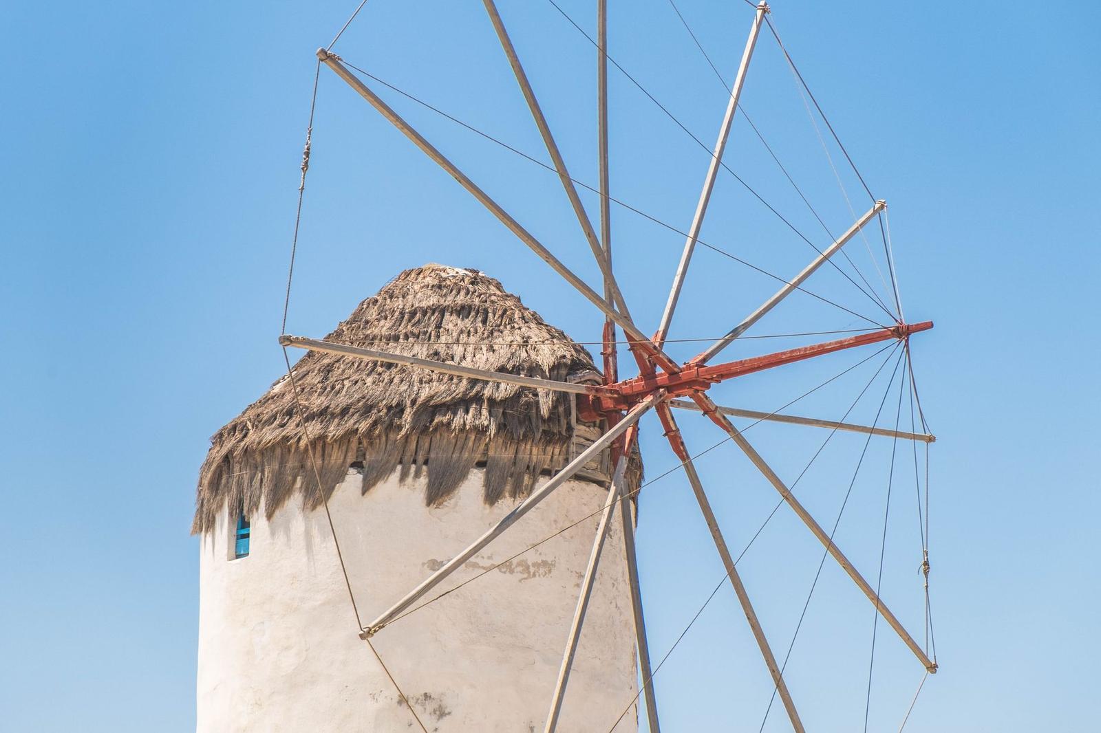 A whitewashed windmill with a thatched cap and bare sails against clear blue sky