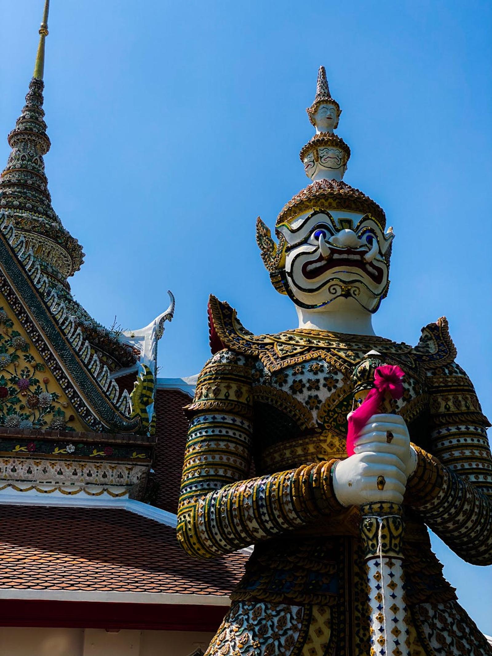 Ornate guardian statue standing before a tiled temple roofline