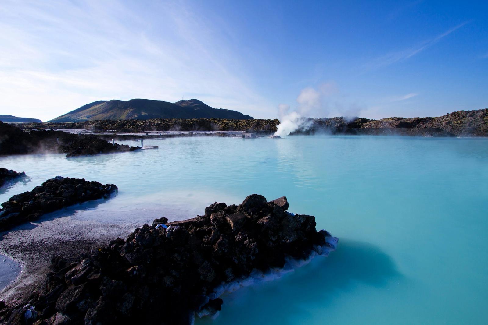 A turquoise geothermal lagoon with steam rising near dark lava rock