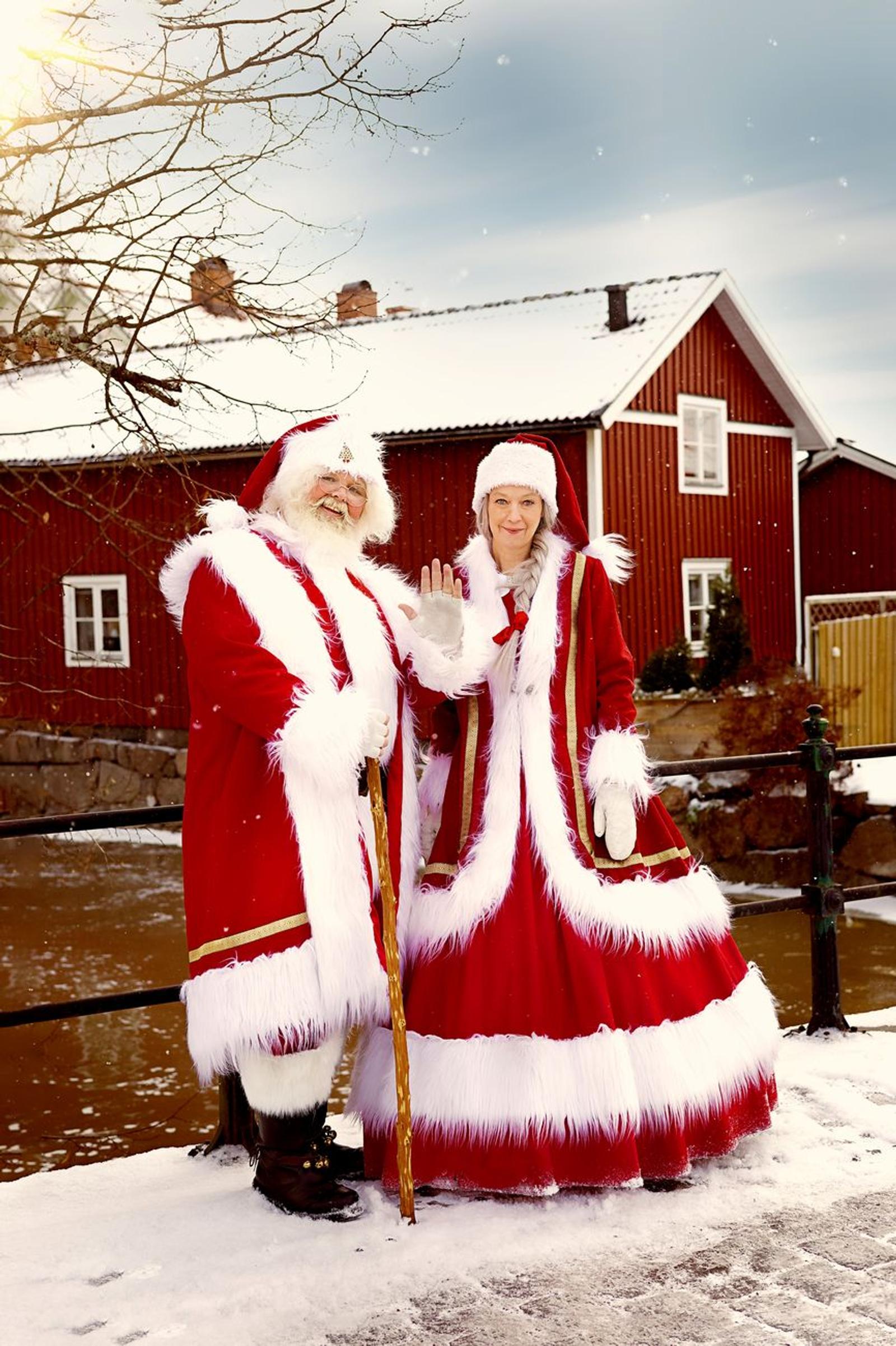 Santa and Mrs Claus in red costumes waving beside a snowy river
