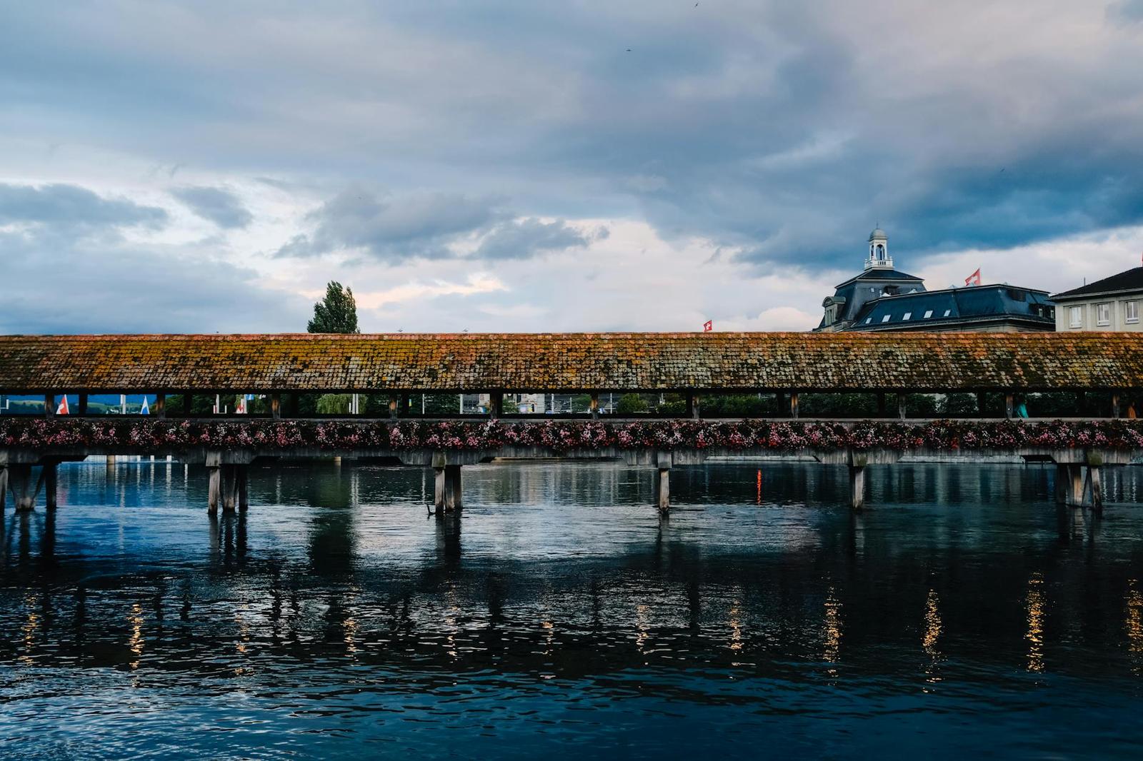Wooden covered bridge reflected in a still river at dusk beside a domed building