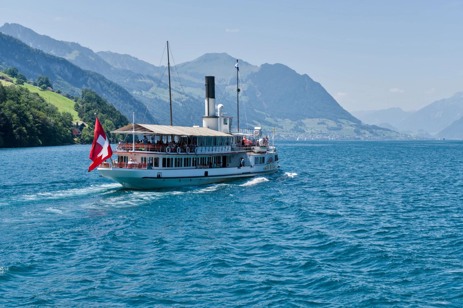 A scenic view of a historic paddle steamer cruising on Lake Lucerne with Swiss flag