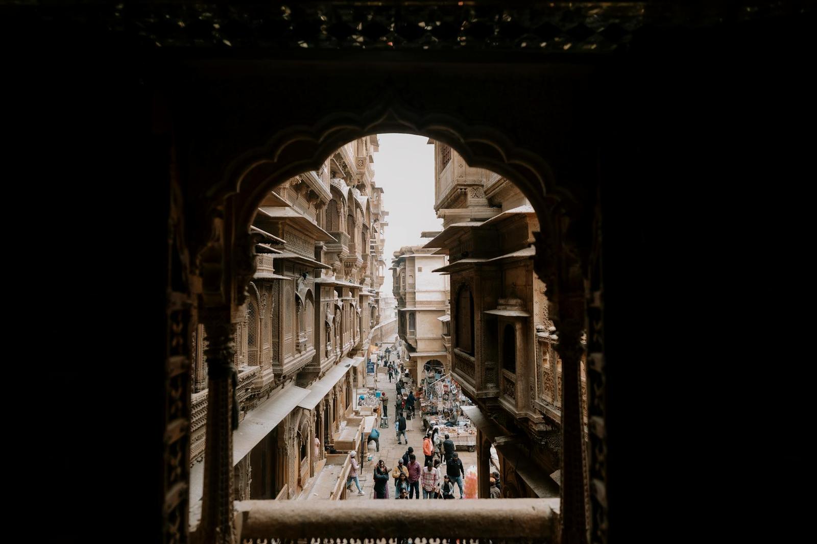 A bustling street in Jaisalmer seen through a historical arched window, conveying heritage and culture