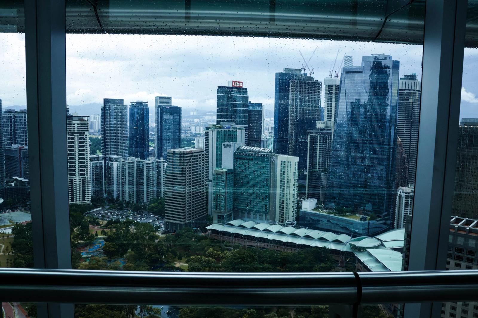 Overcast view of Kuala Lumpur's modern skyline through a rain-speckled window