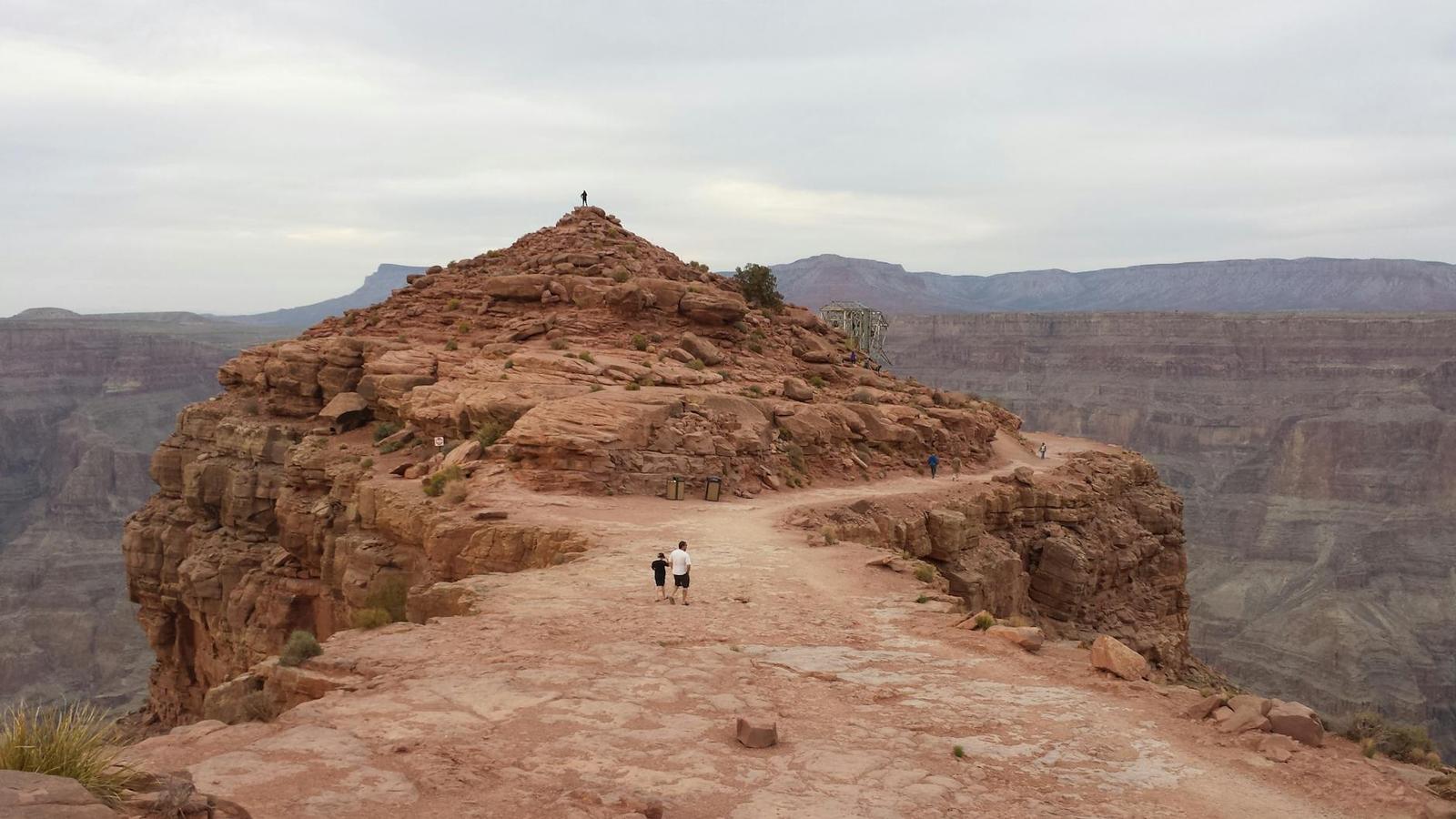 Hikers on a narrow rock outcrop overlooking a vast layered canyon