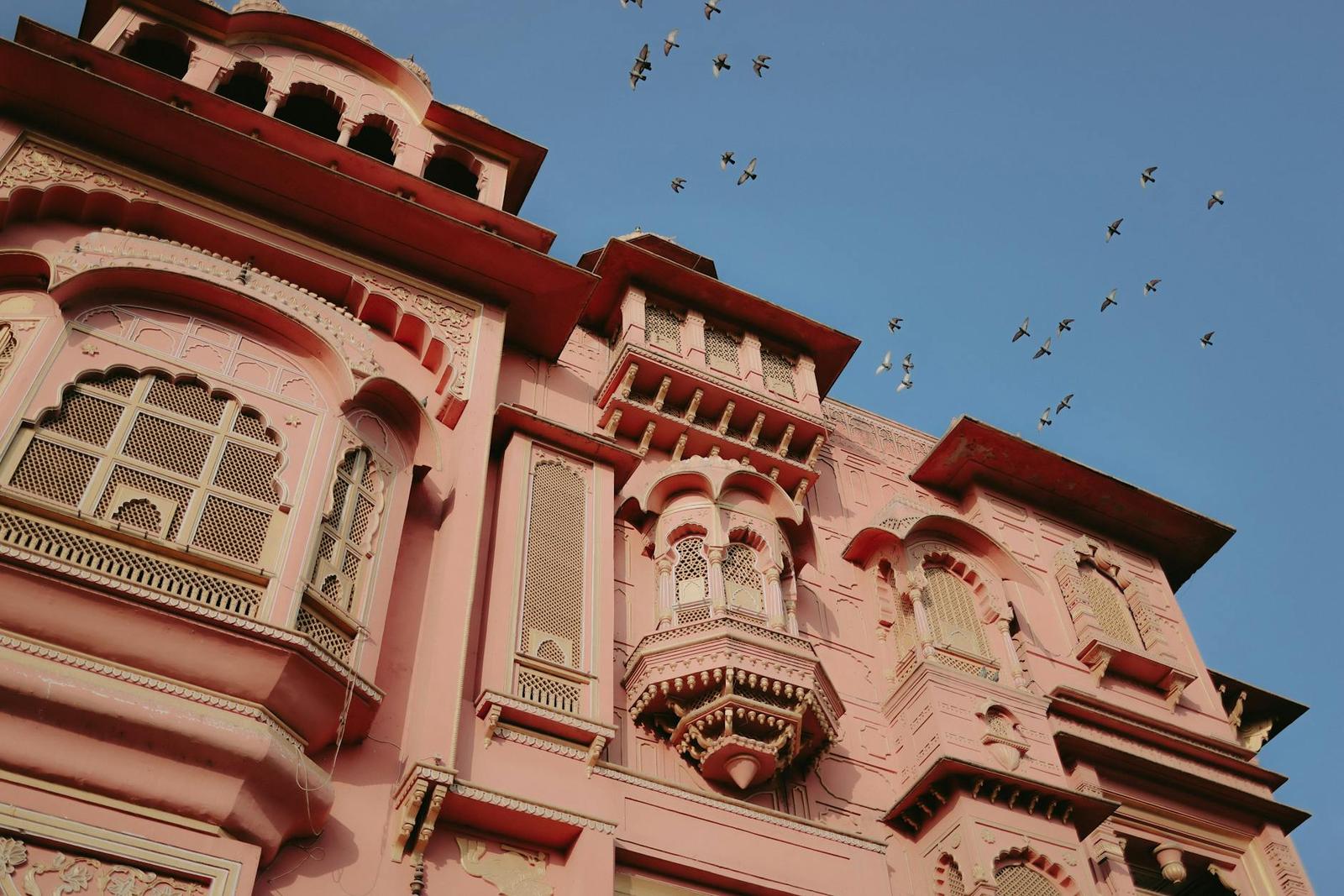 A pink sandstone building facade with balconies and circling birds