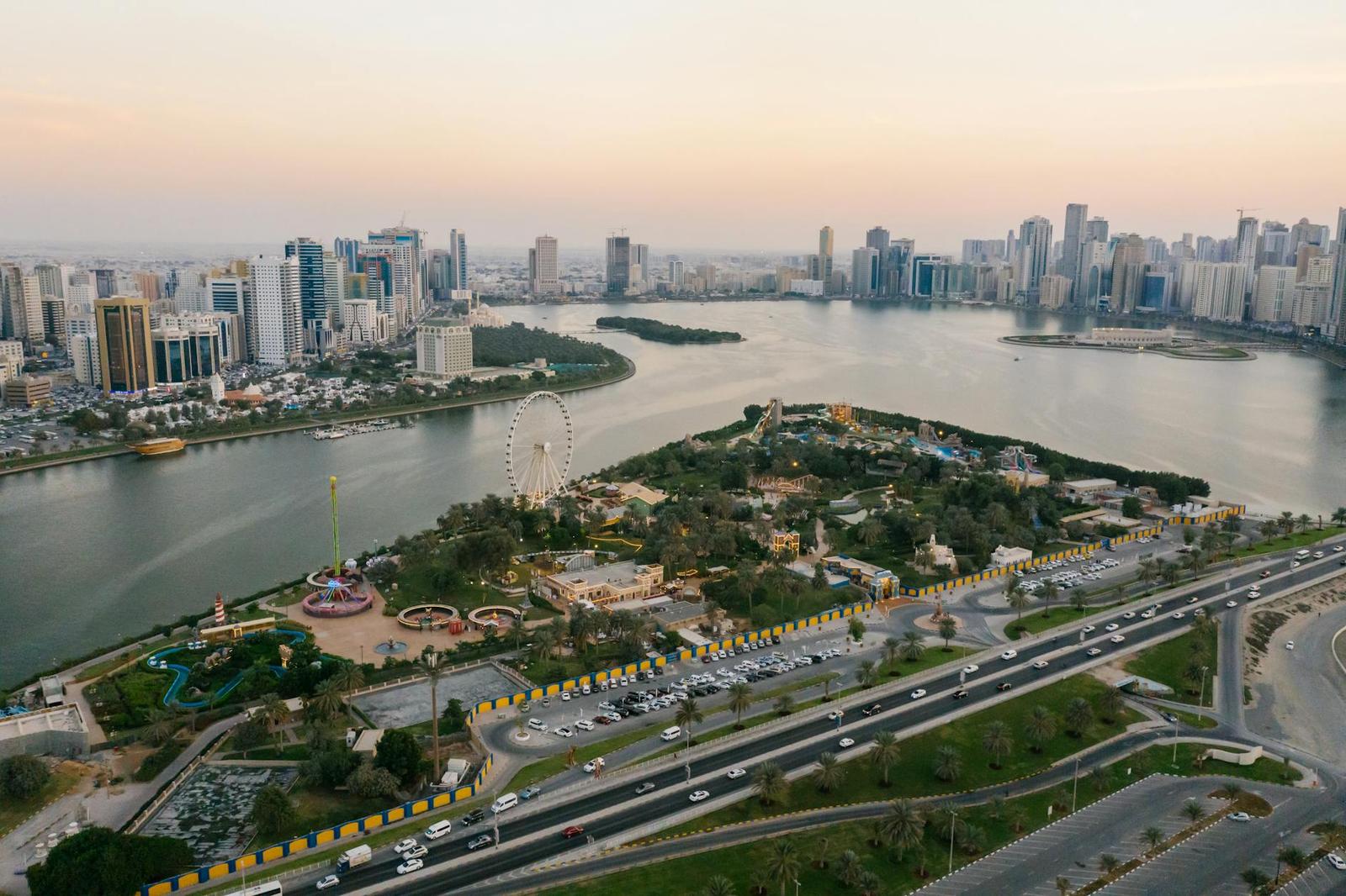 An aerial view of a park island with a ferris wheel between two city shores