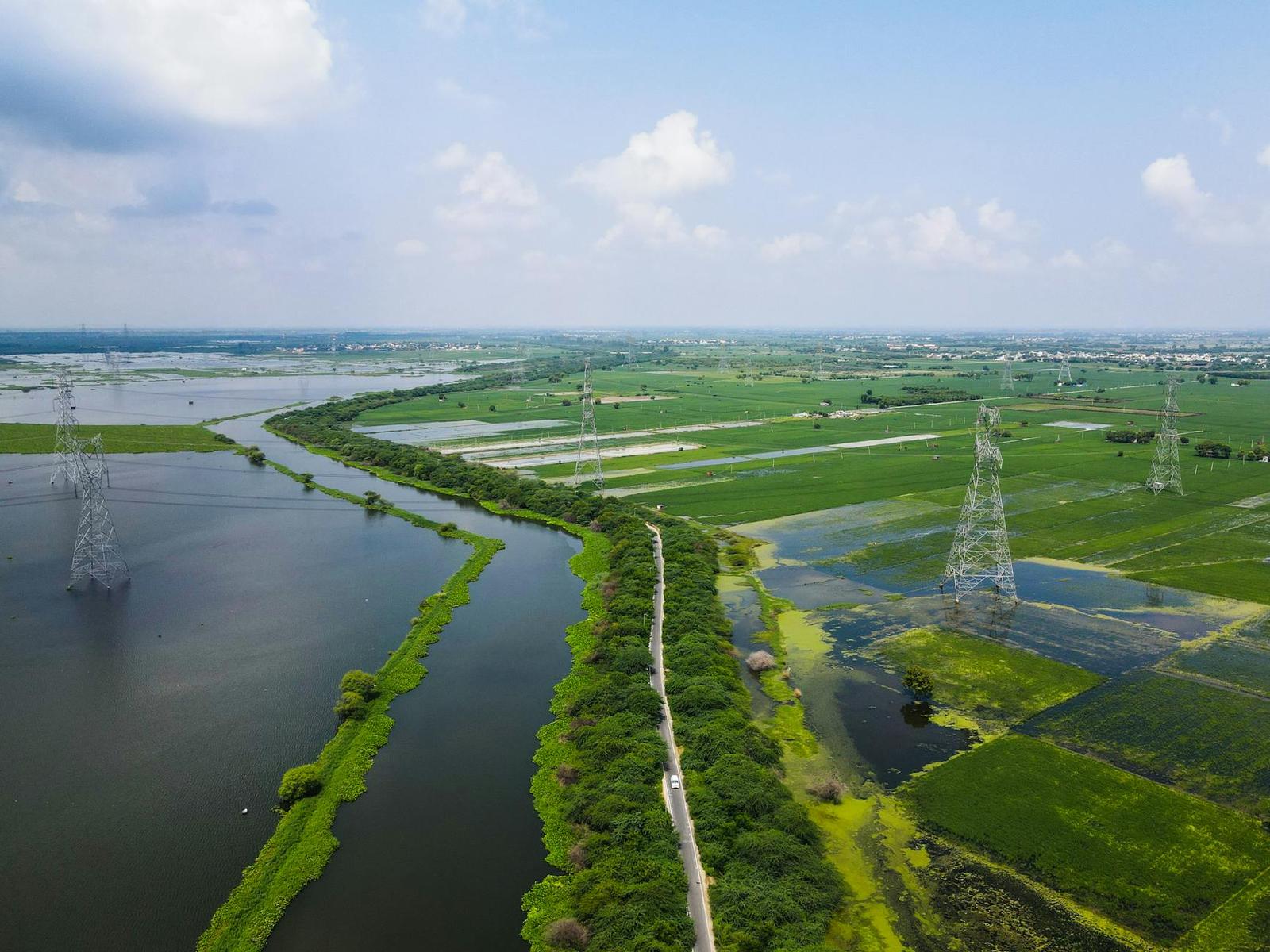 Aerial view of a river winding through green farmland under power lines