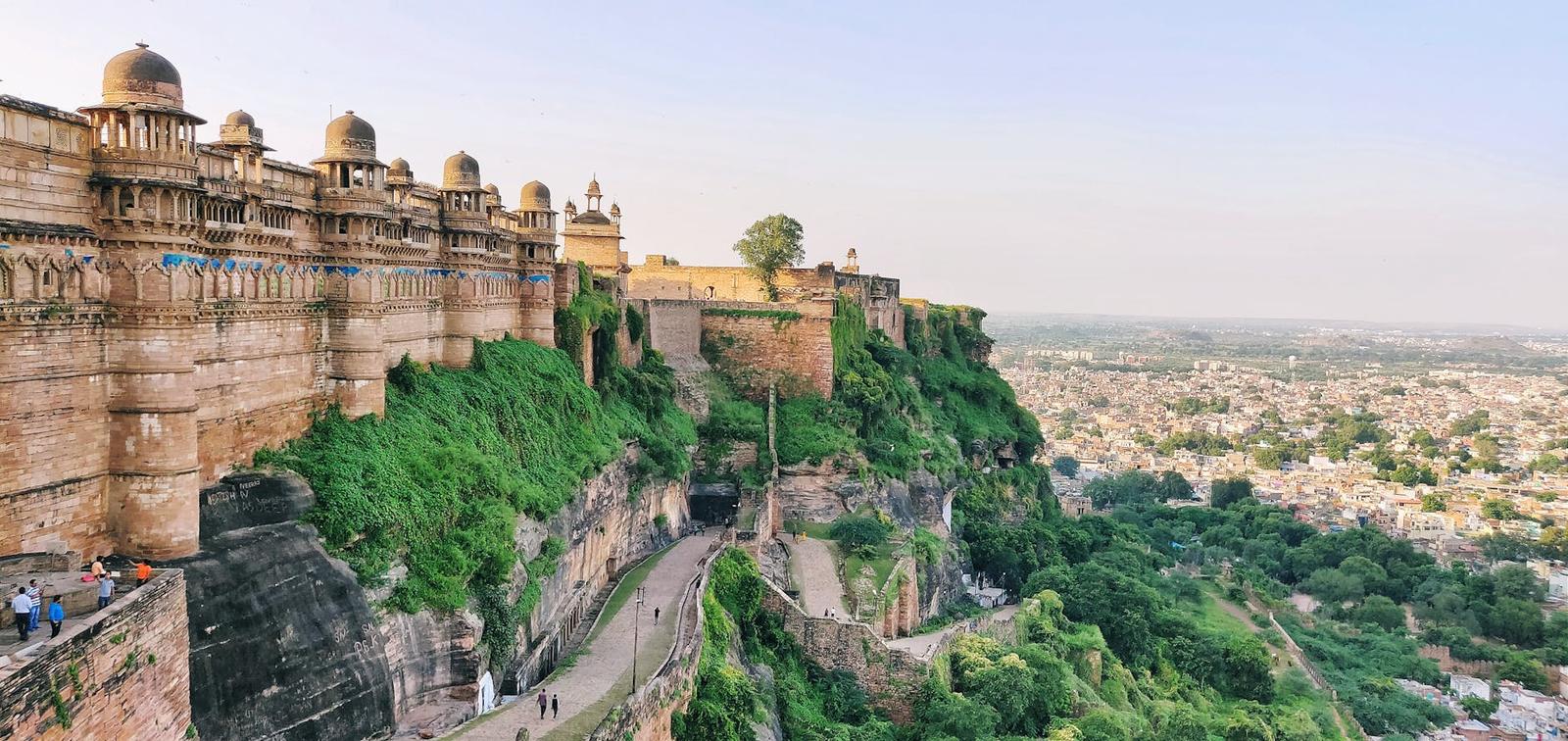 Hilltop fortress with fortified walls overlooking a green ravine and distant city