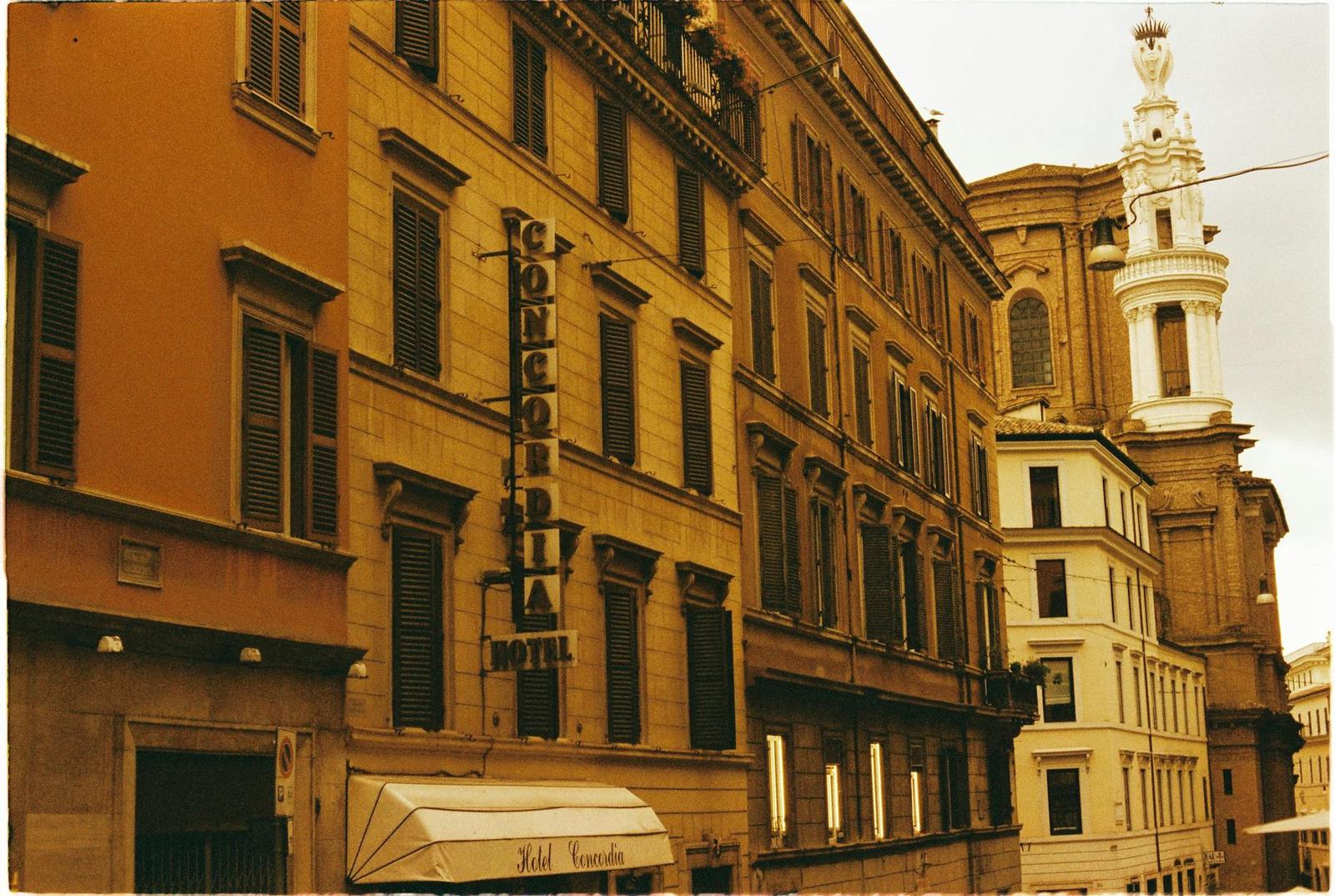 A row of ochre hotel buildings on a narrow street with a church tower beyond