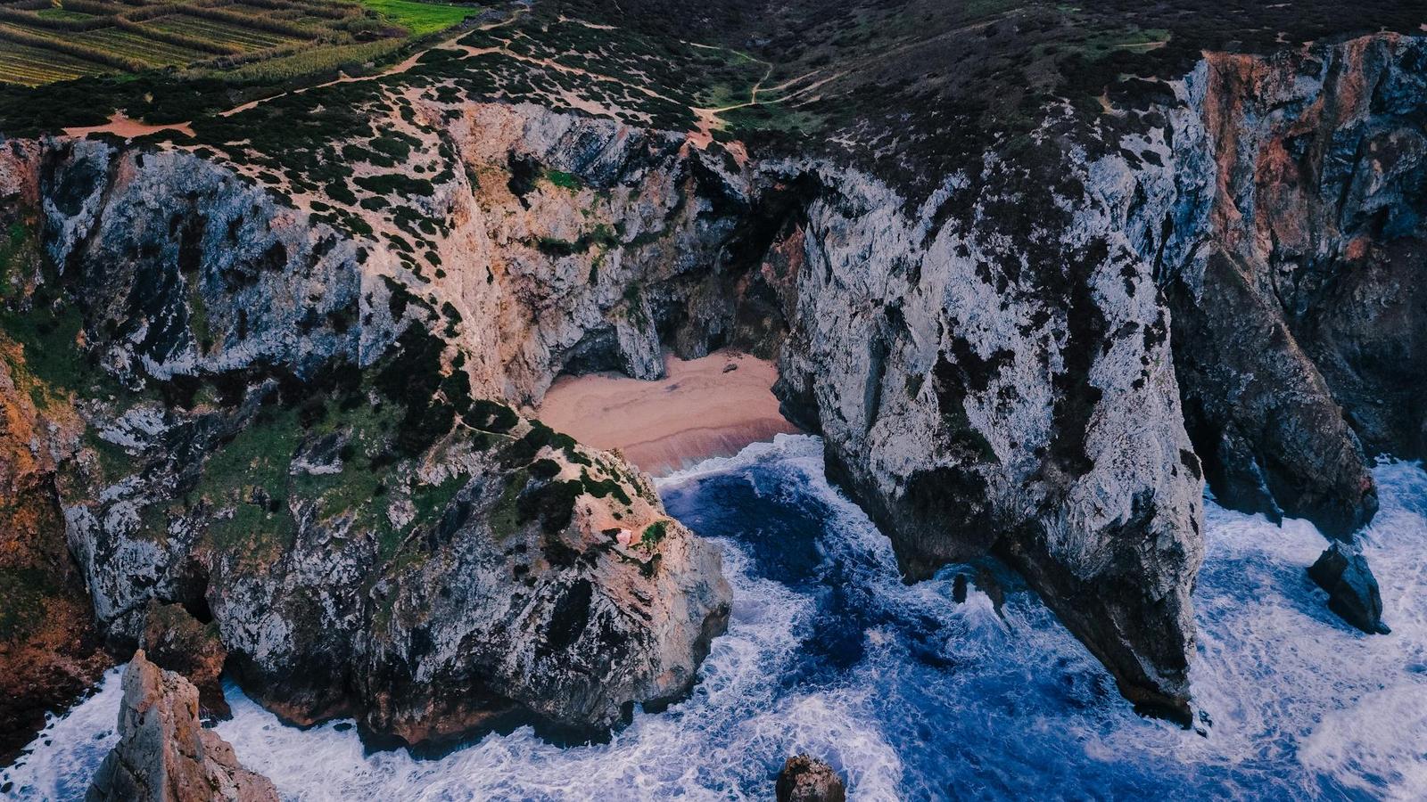 Aerial view of a hidden sandy cove tucked between towering sea cliffs