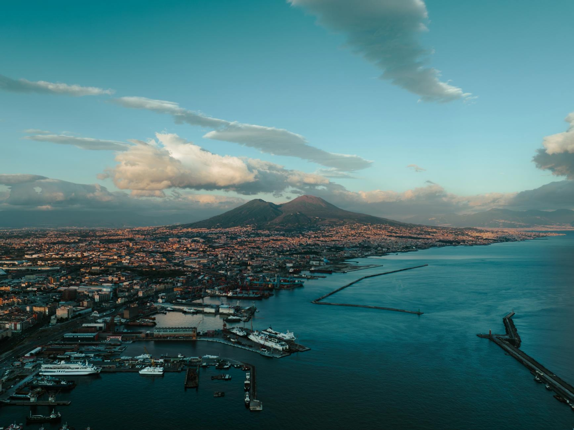 Aerial view of a harbour city beneath a conical volcano at dusk
