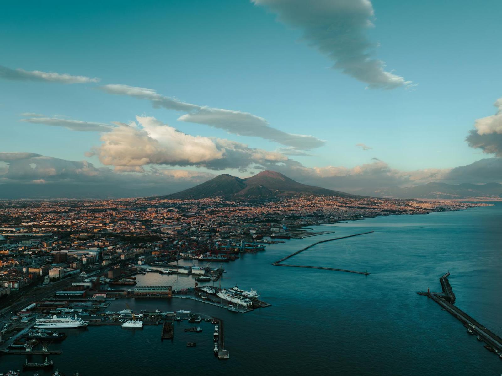 Aerial view of a harbour city beneath a conical volcano at dusk