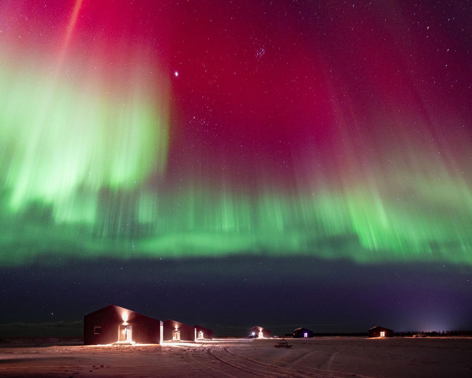 Vivid red and green aurora glowing over remote cabins at night