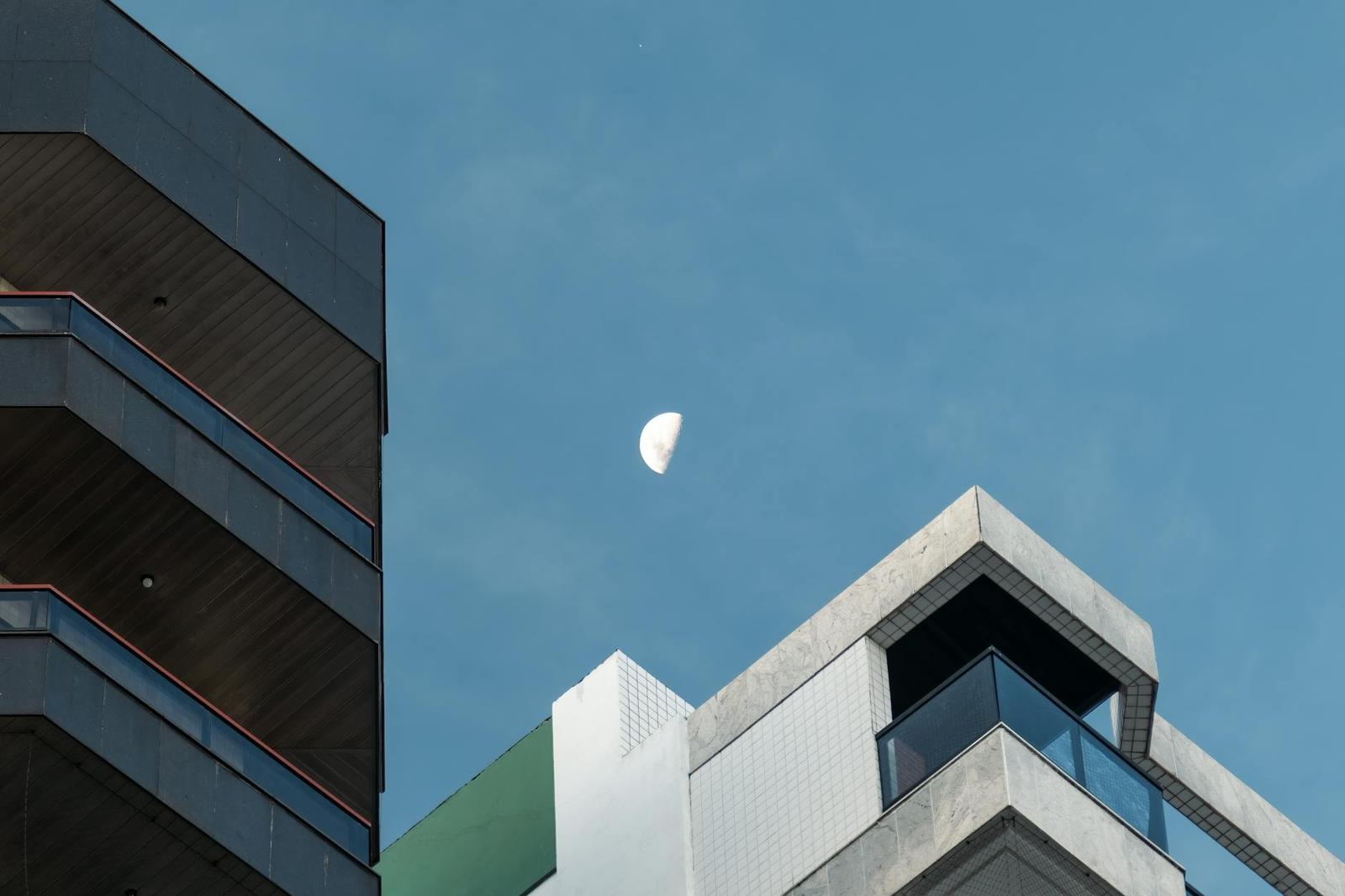 A crescent moon over the sharp corner of a modern glass building