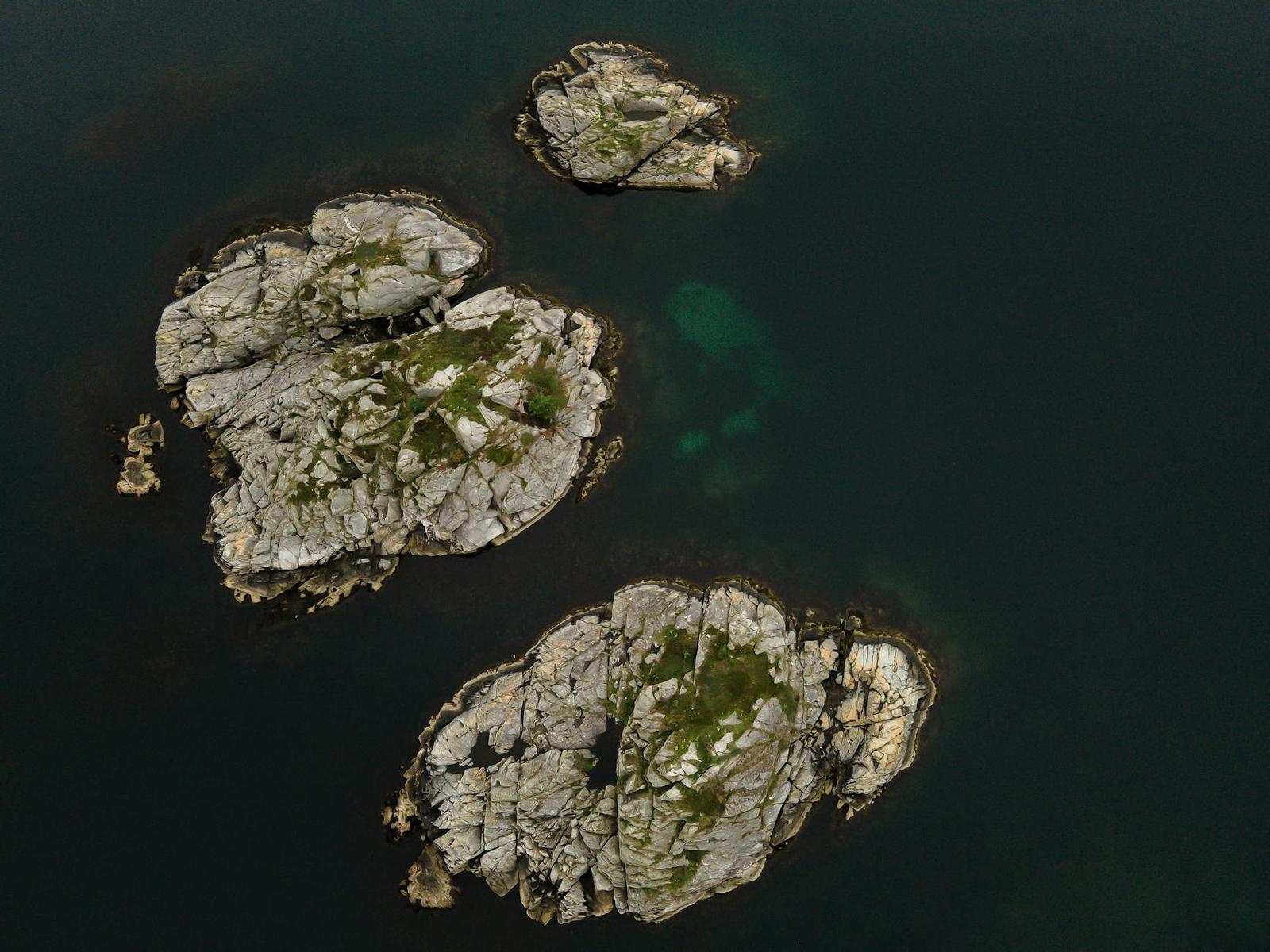 Aerial view of small moss-covered granite islets in dark still water