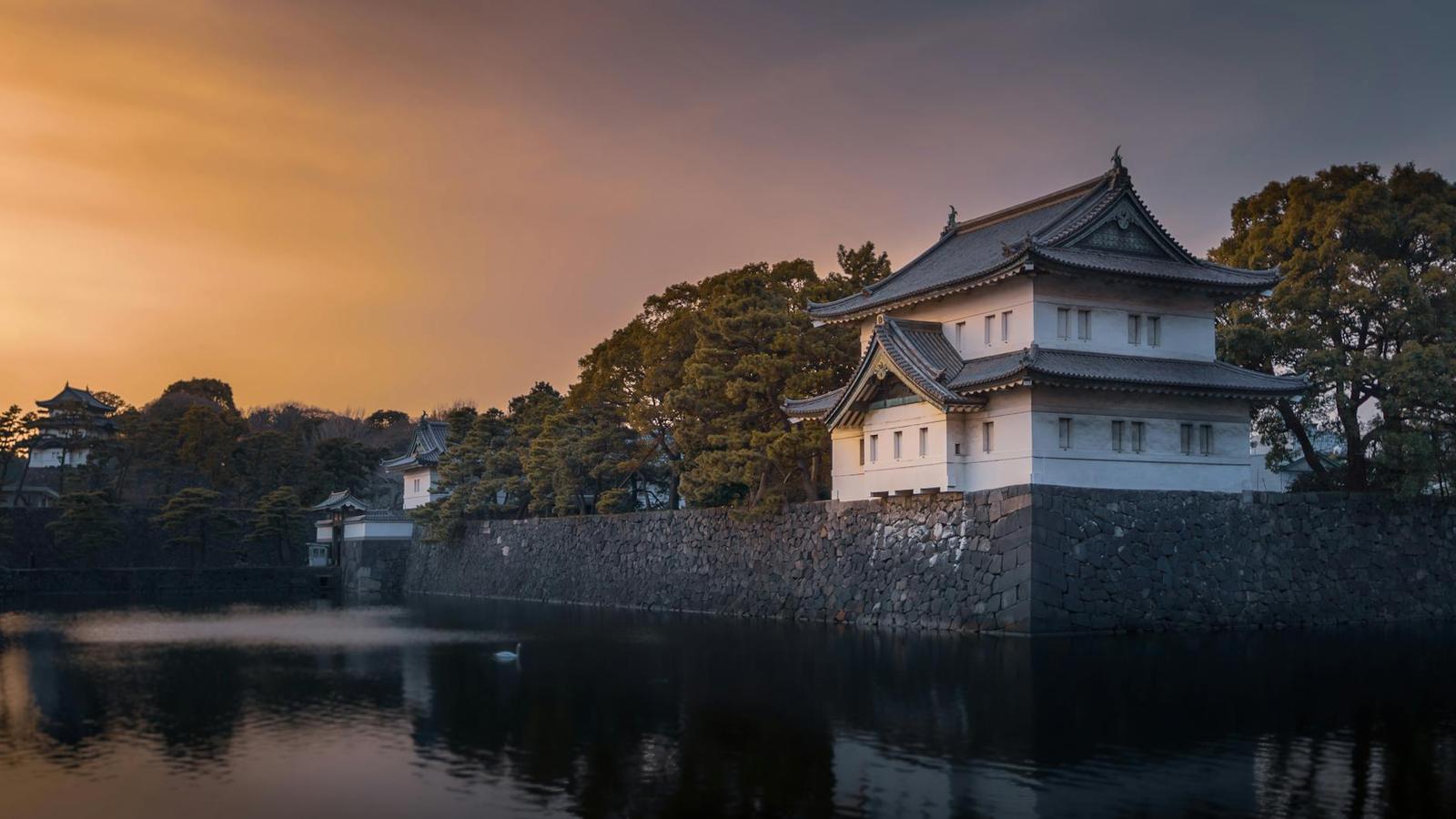 A stone-walled castle turret beside a moat lit by a dusk sky