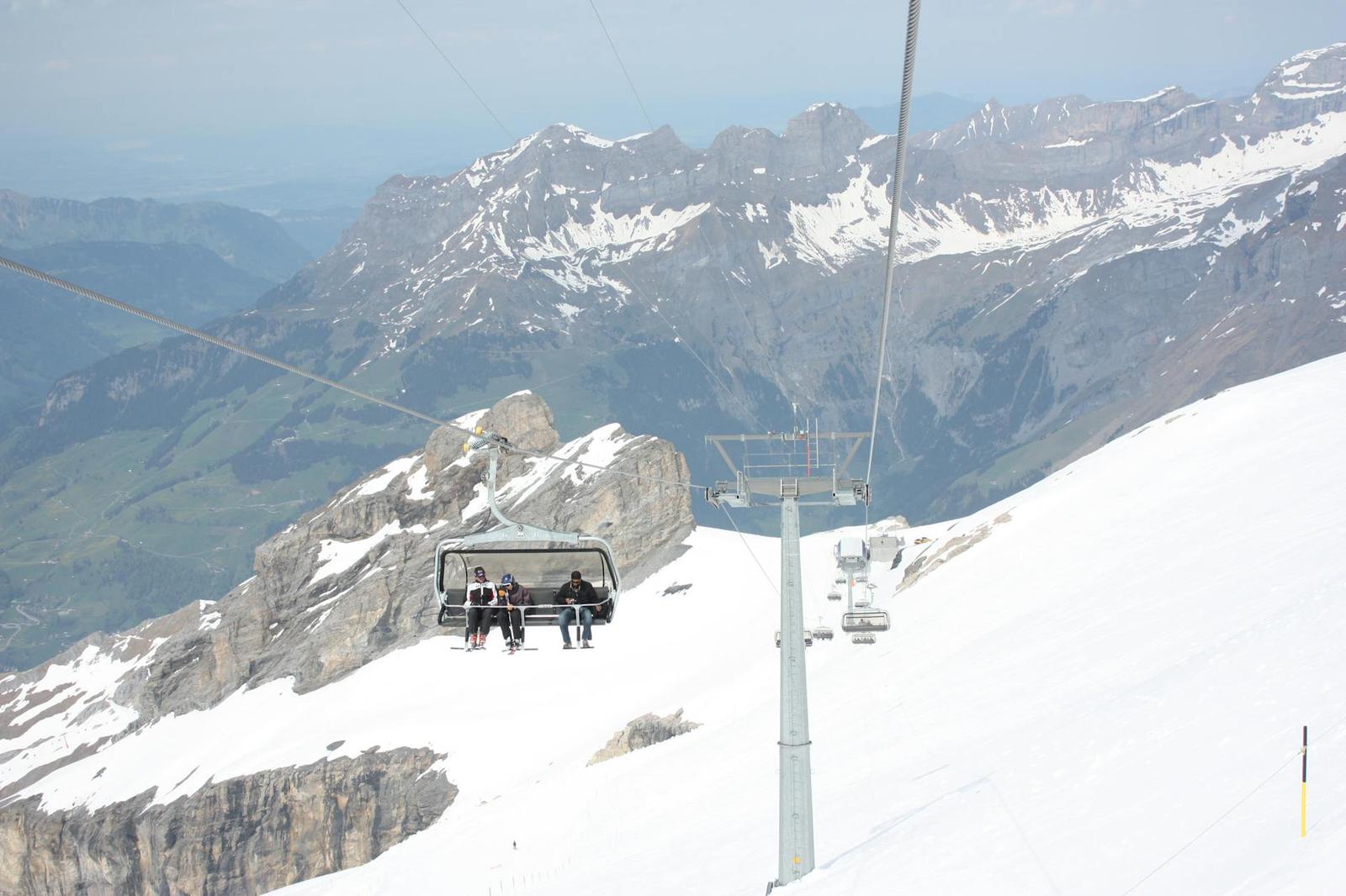 Two passengers riding a chairlift over a snowy alpine slope