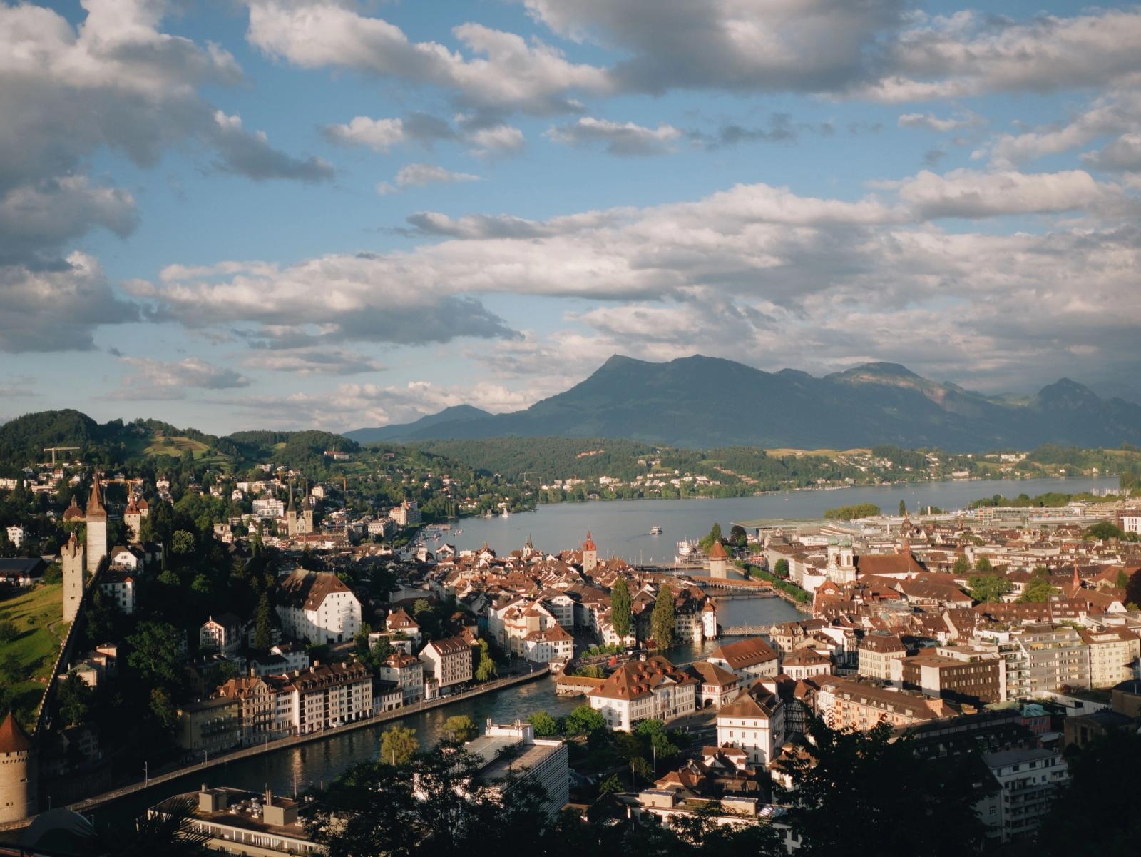 Elevated view of a riverside old town with mountains rising beyond a lake