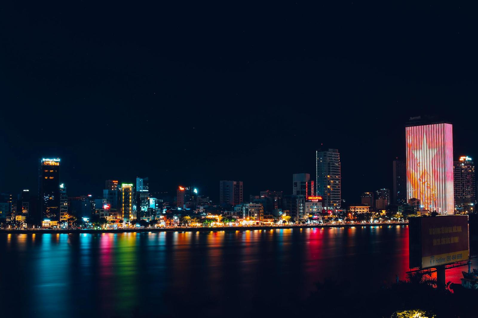 A riverfront city skyline lit up in colorful reflections at night