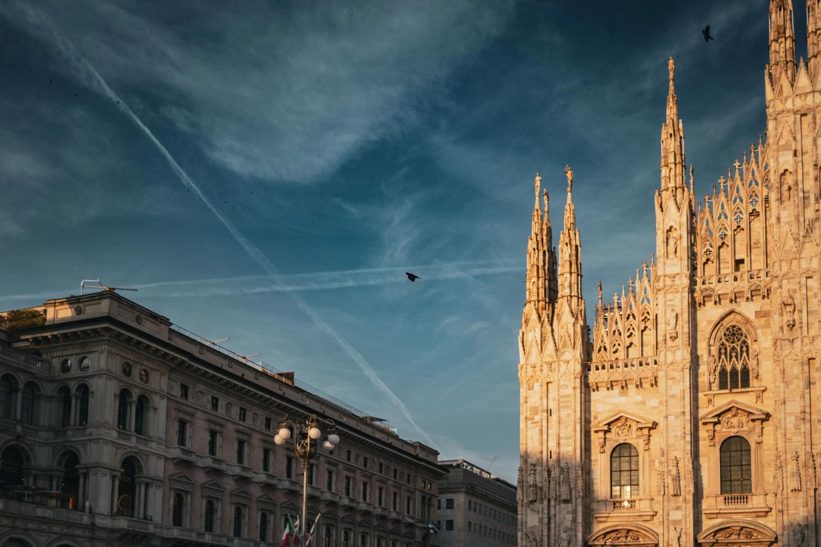 Captivating evening shot of the Milan Cathedral with clear skies and birds in flight, capturing its intricate Gothic architecture