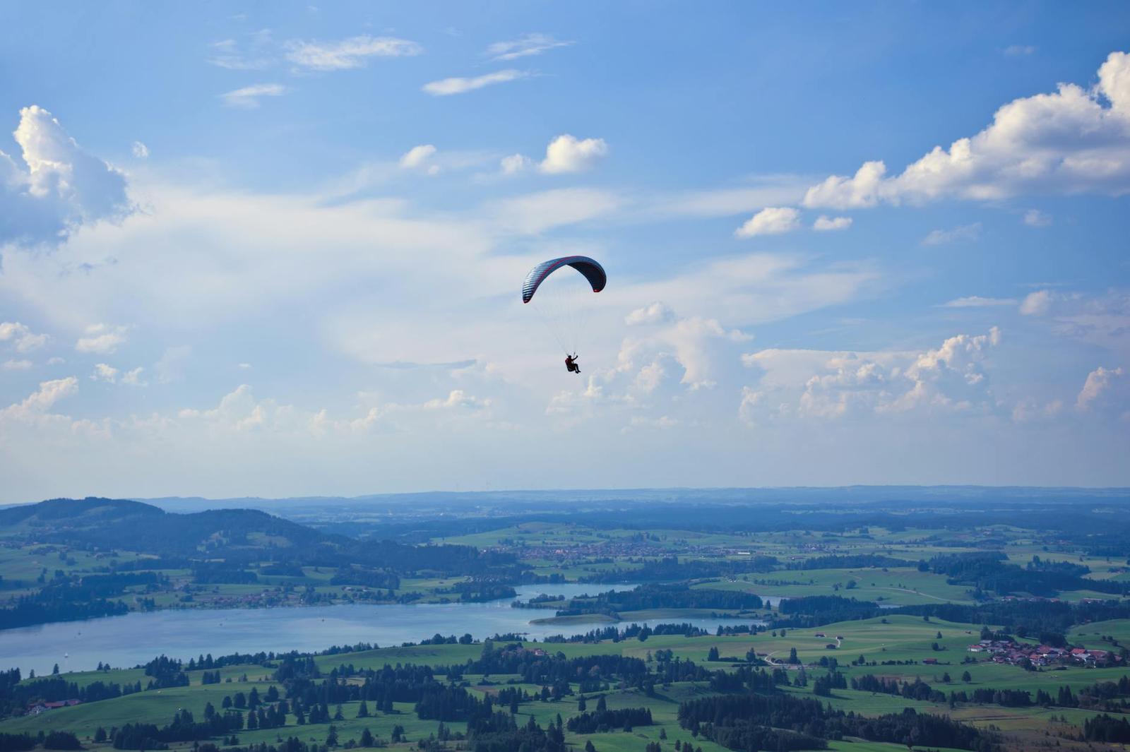 A paraglider drifts above a green valley and lake below