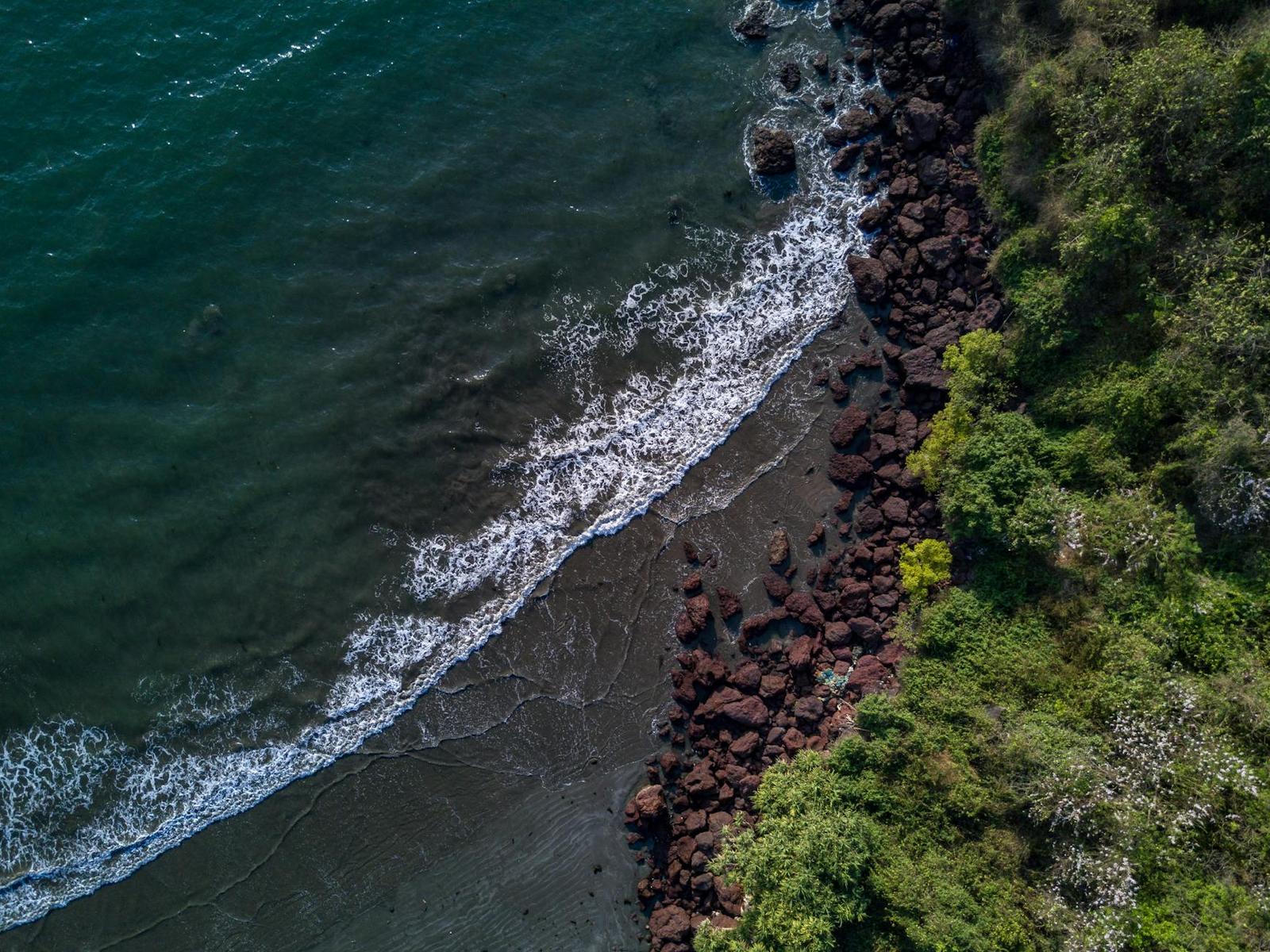 Aerial view of turquoise waves breaking over a rocky green shoreline