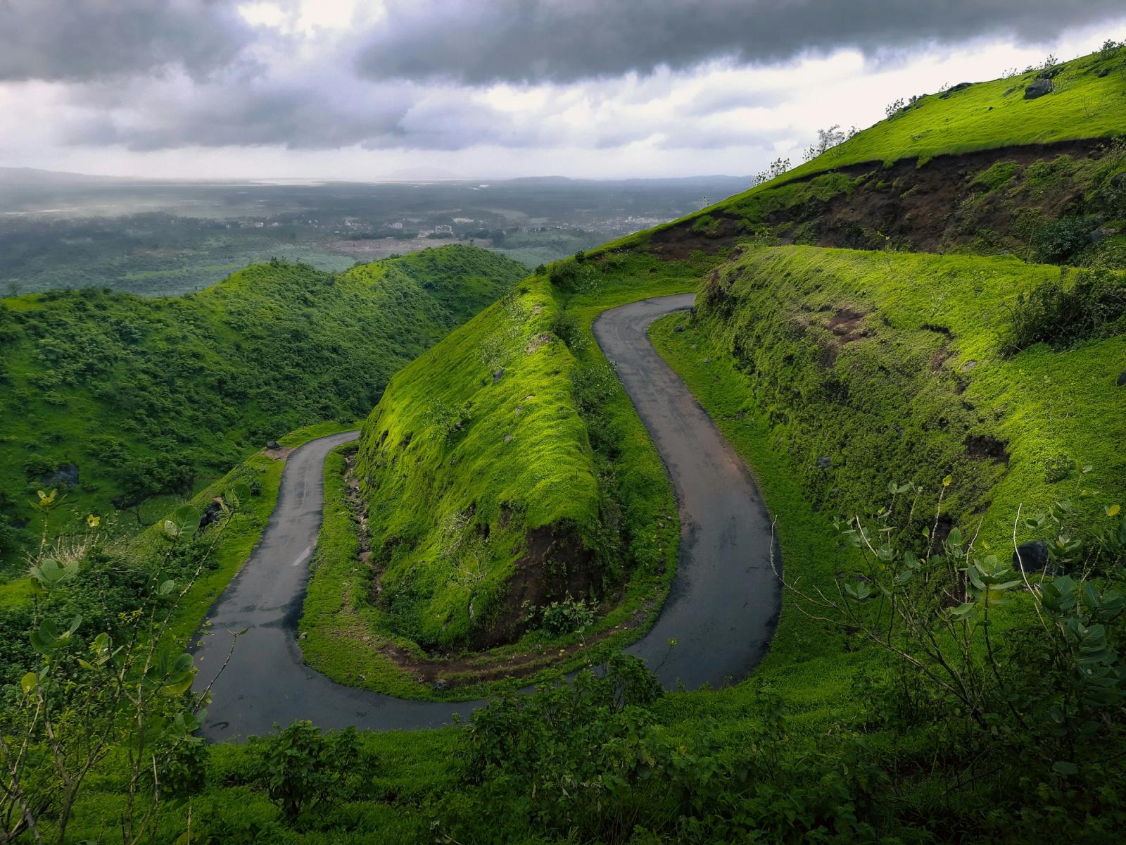 Scenic view of a winding road cutting through lush green hills under a cloudy sky in India