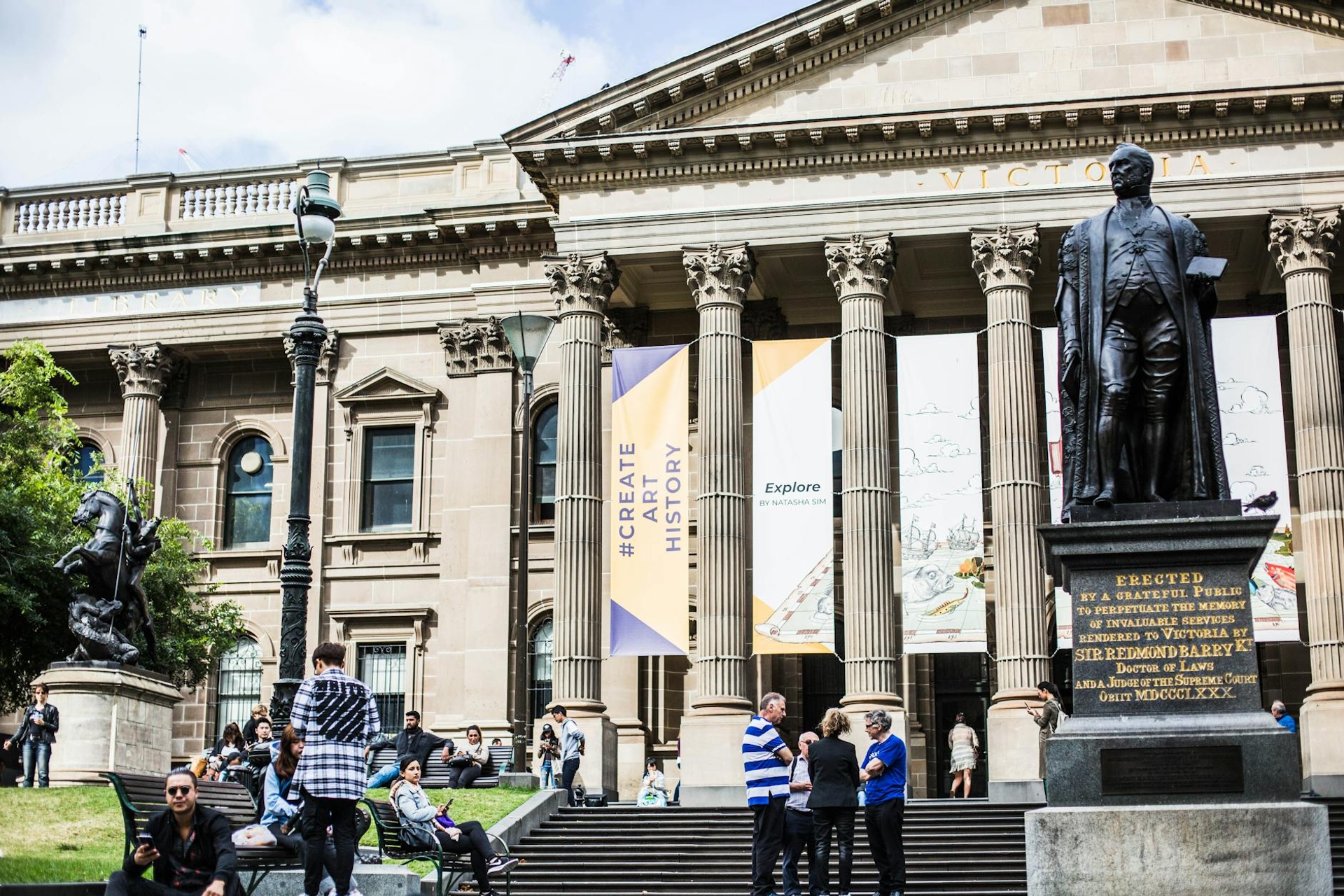 Neoclassical colonnaded building with a statue in front and visitors on the steps