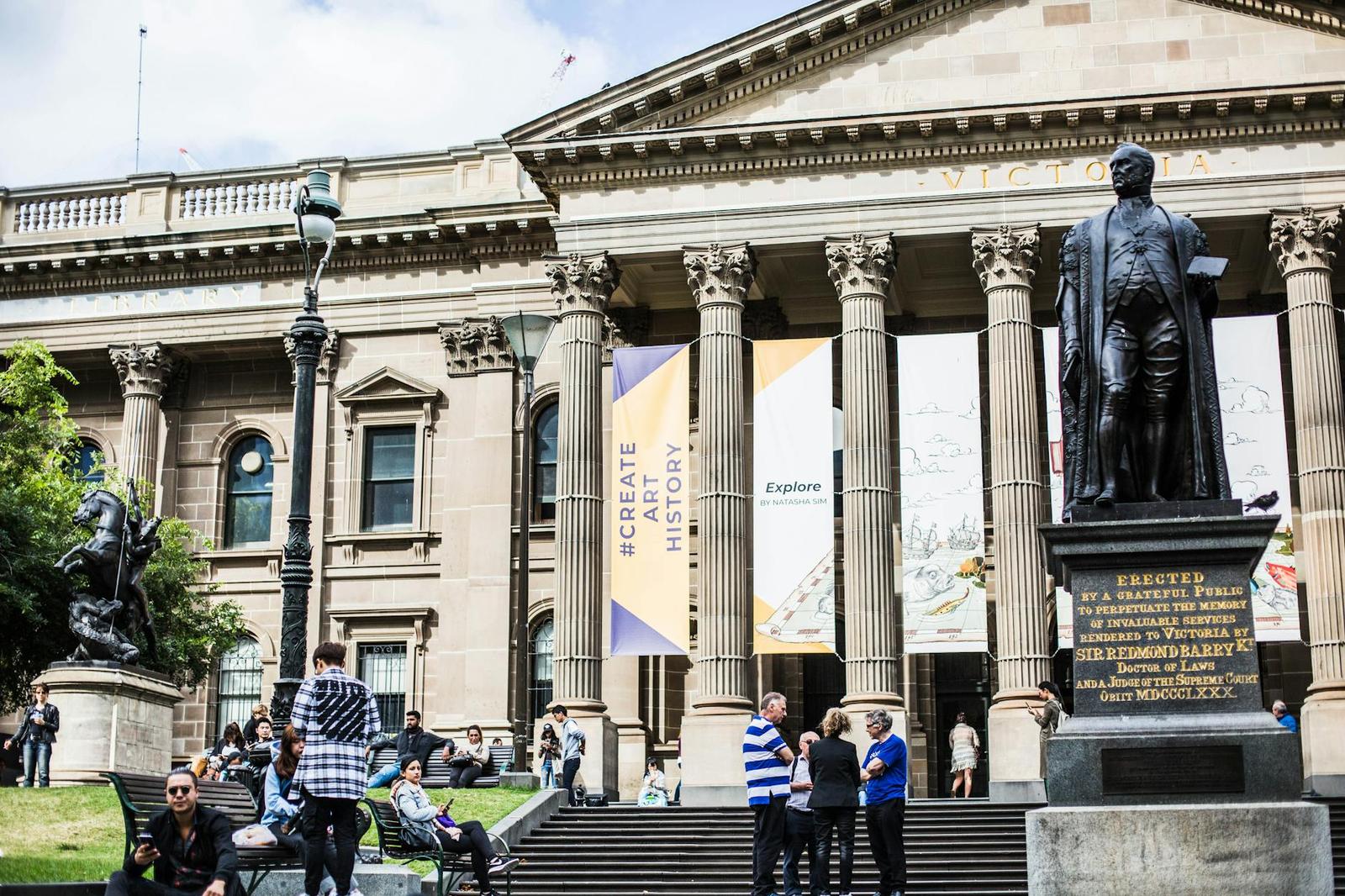 Neoclassical colonnaded building with a statue in front and visitors on the steps