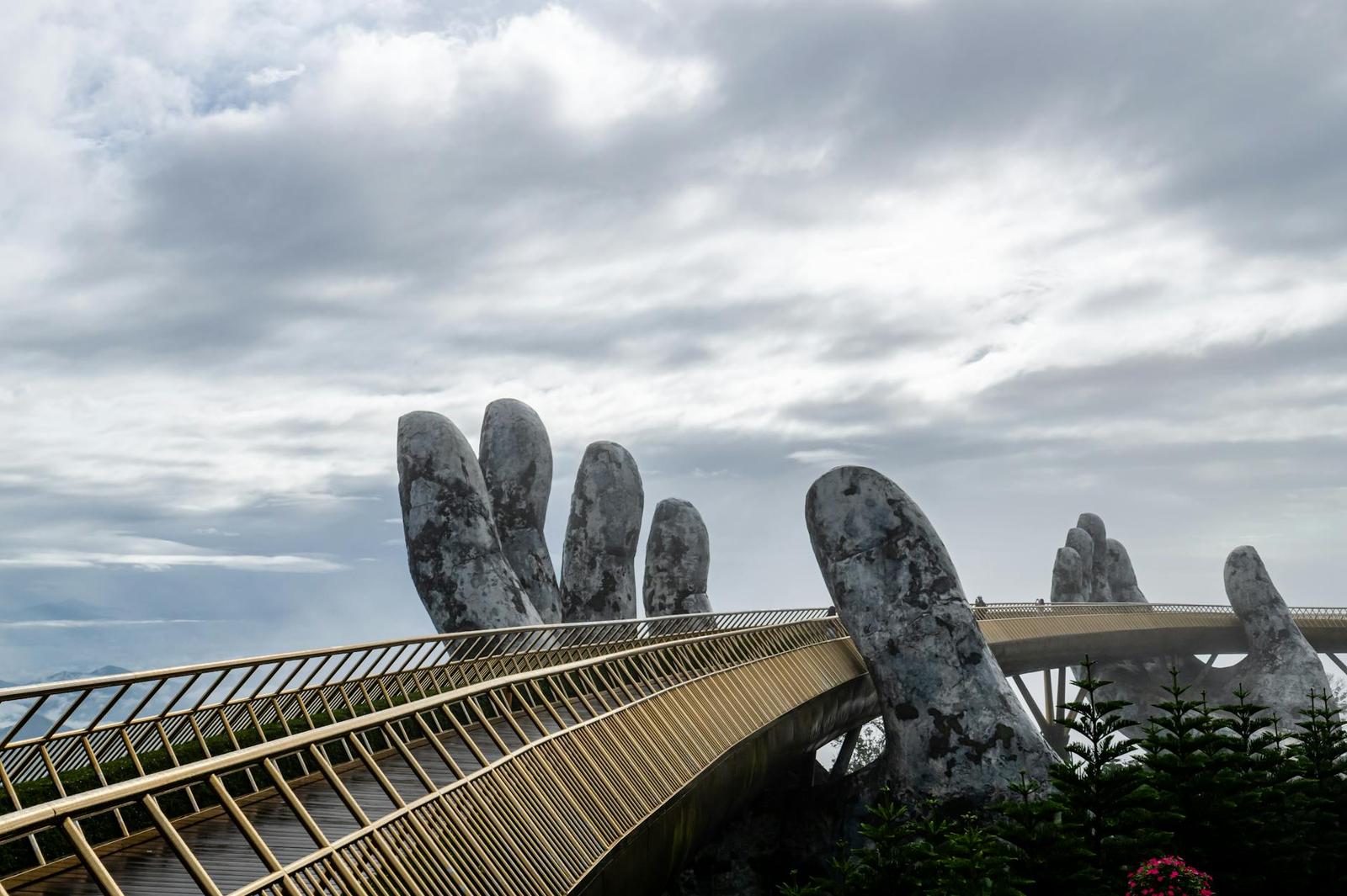 Giant stone hand sculptures lifting a golden walkway into misty hills