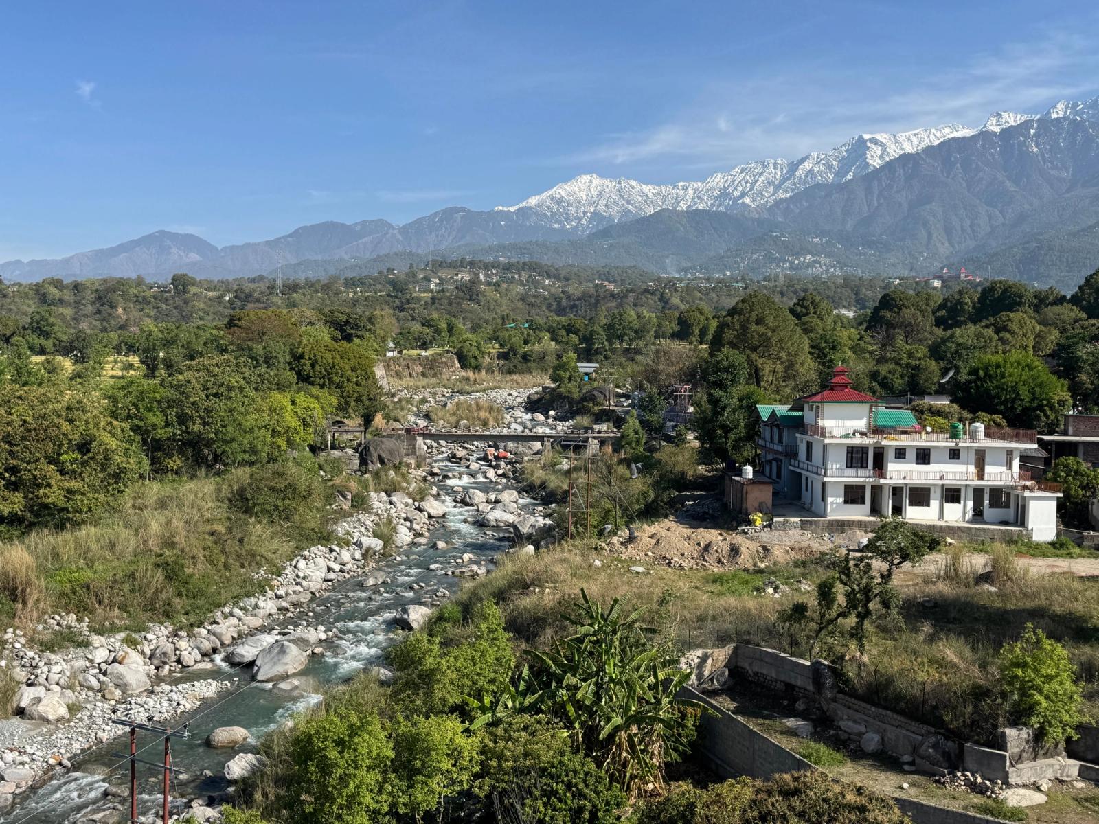 Picturesque landscape of Dharamshala, India showcasing a river, lush greenery, and snowy mountains